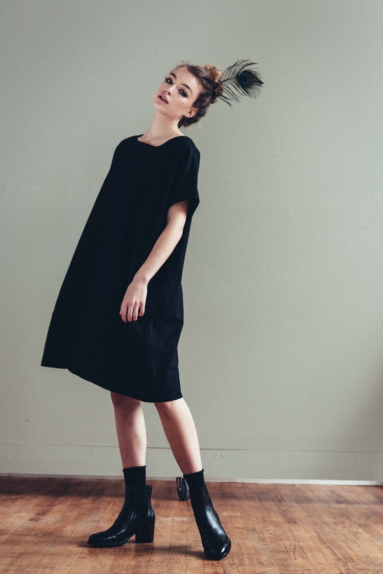 a model is standing in an editorial photographer studio room wearing a black tunic dress.jpg