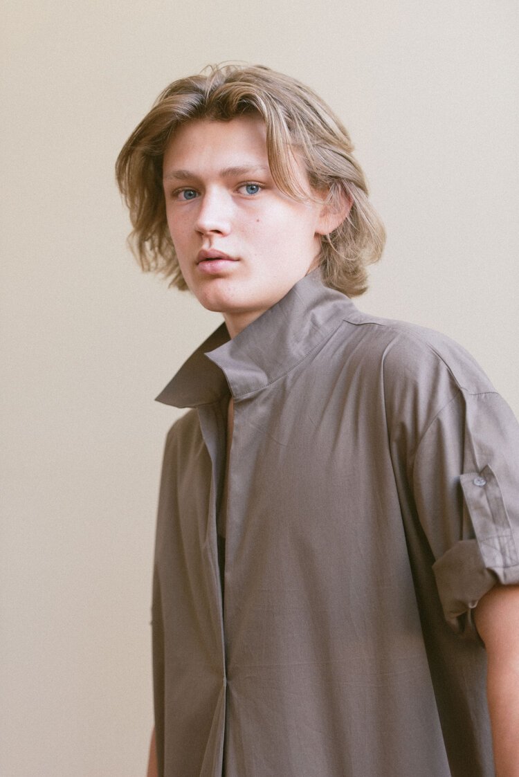 A young man in a brown shirt is posing for an editorial photo.jpg
