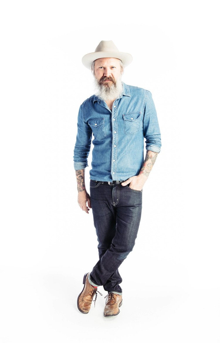 An indoor editorial photograph featuring a bearded man in jeans and a hat.jpg