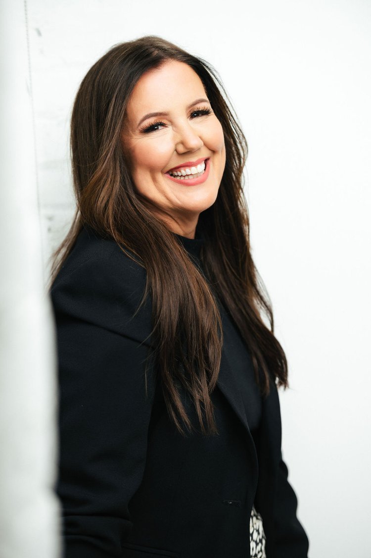 a woman in a black coat posing for headshots with a smile.jpg