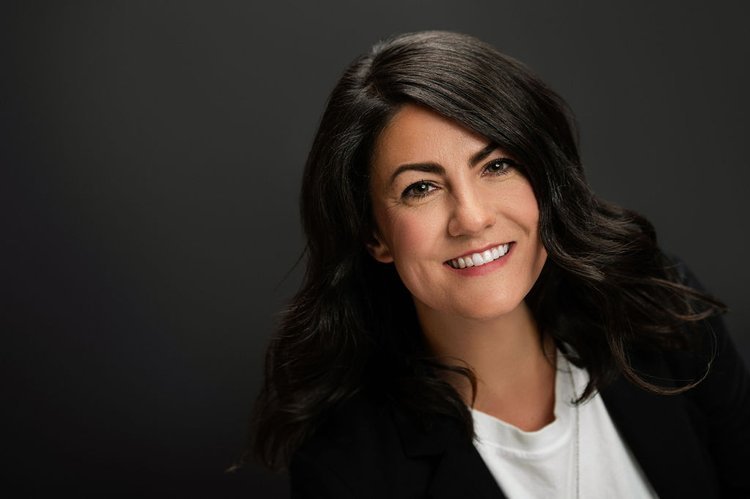 A woman in a professional black blazer and crisp white shirt exudes confidence and warmth in her LinkedIn headshot..jpg