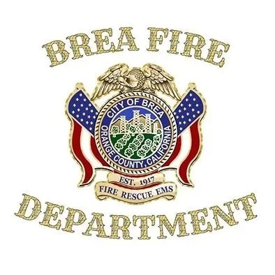 A middle-aged man with gray hair in a black fire department uniform, standing against a black background, with a badge on his chest and a patch on his shoulder.