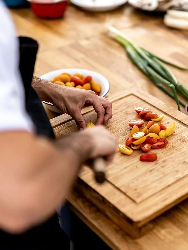 Someone chopping cherry tomatoes on a wooden cutting board in a kitchen area.