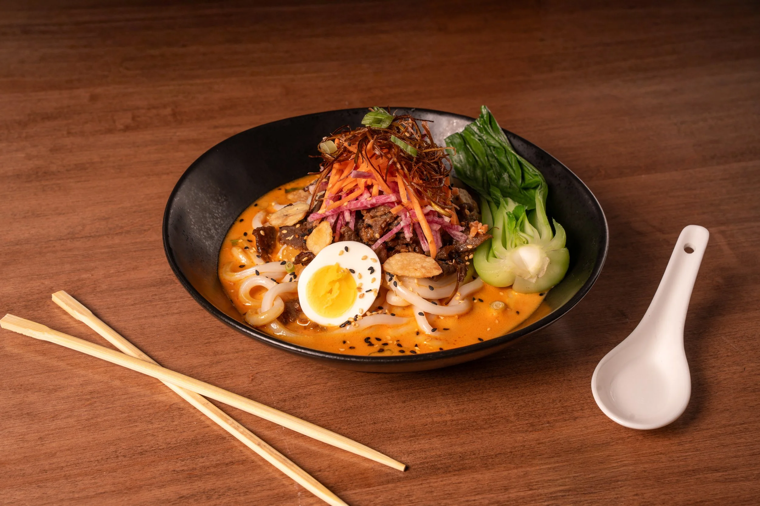 Japanese Beef Noodles: shaved AAA striploin steak, japanese curry, thick udon noodles, carrots, bok choy, radish, crispy garlic, toasted sesame, green onions. 