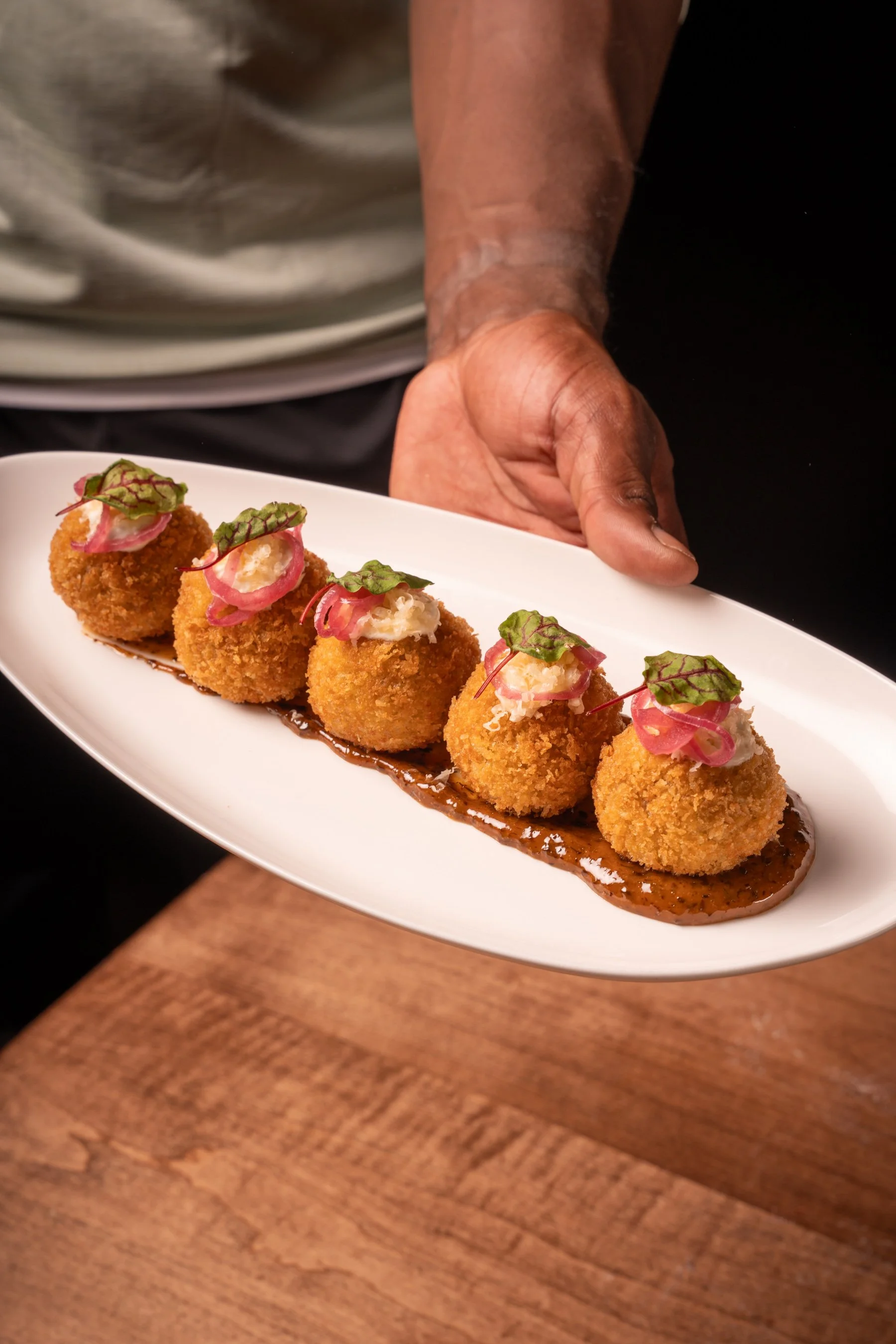 French Onion Croquettes: crispy caramelized onion croquettes, aged cheddar, smoked gouda, pickled onions, black aioli, creme fraiche