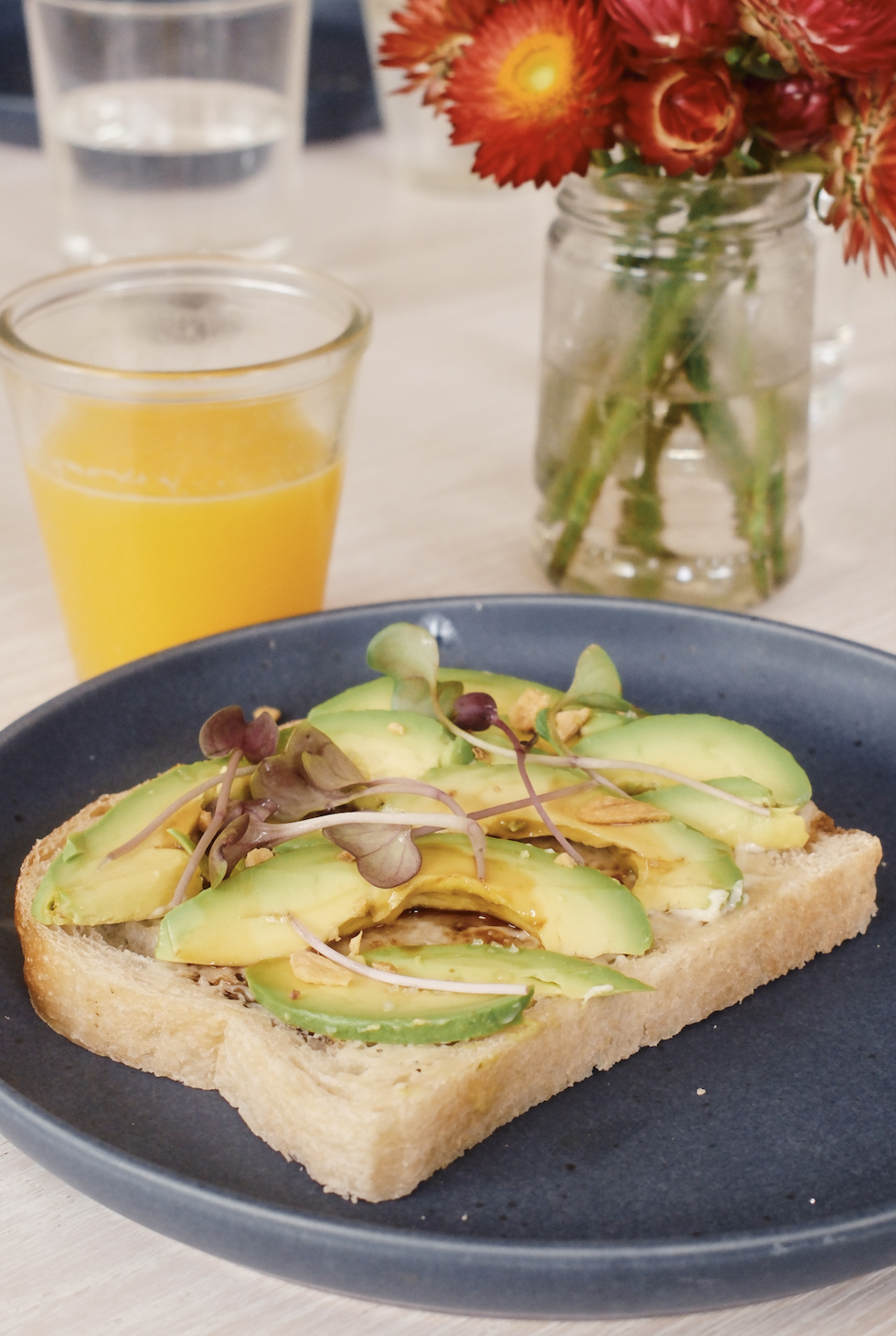 avocado toast with fresh squeezed orange juice and cut flowers on the kitchen table