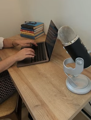 residency guest on computer with microphone and stack of books with glasses on top