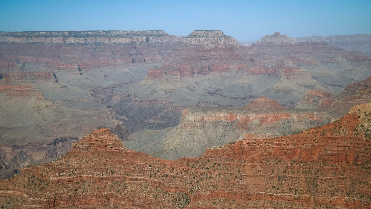 Layered canyon walls and red rock ridges stretching across a broad landscape beneath blue sky.