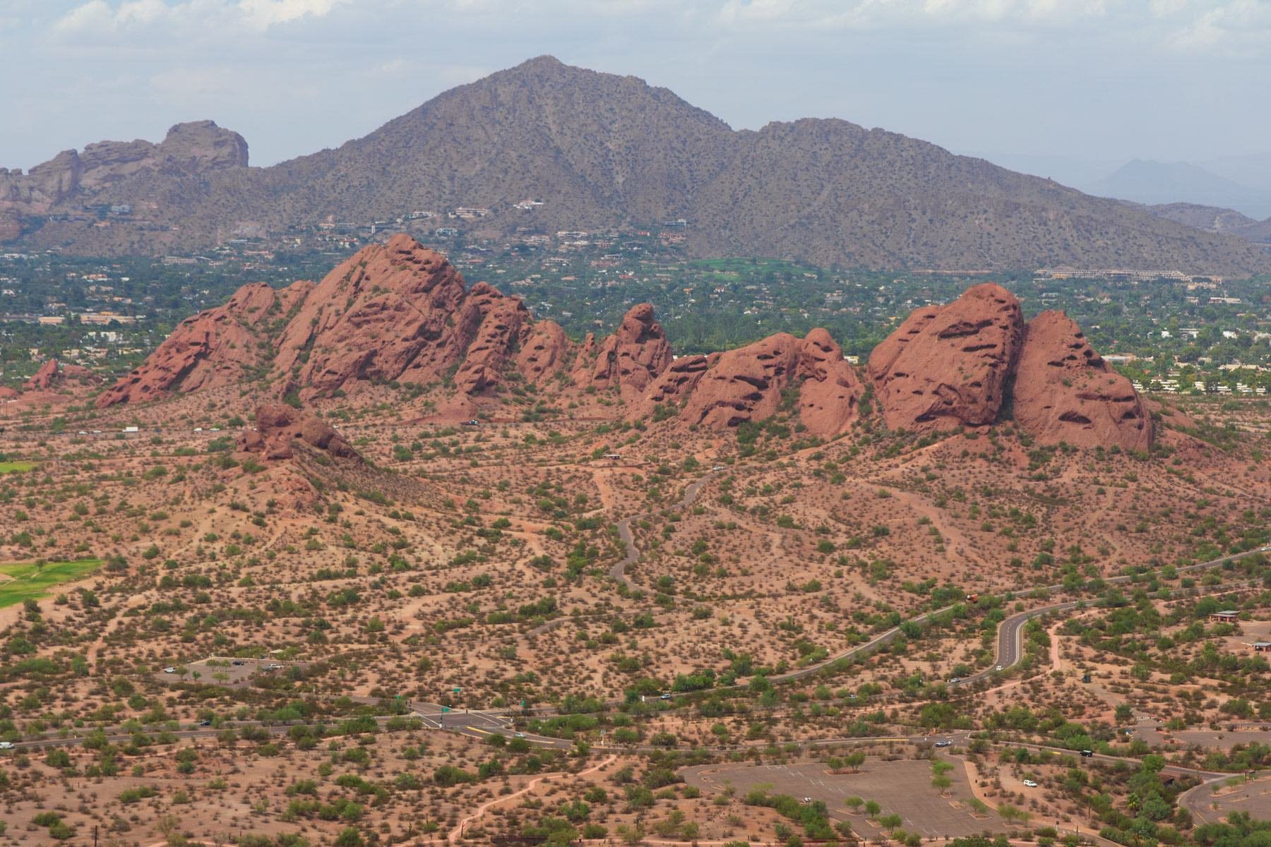 Elevated Arizona landscape photograph of the red sandstone Papago Buttes with Camelback Mountain rising across the Phoenix horizon.