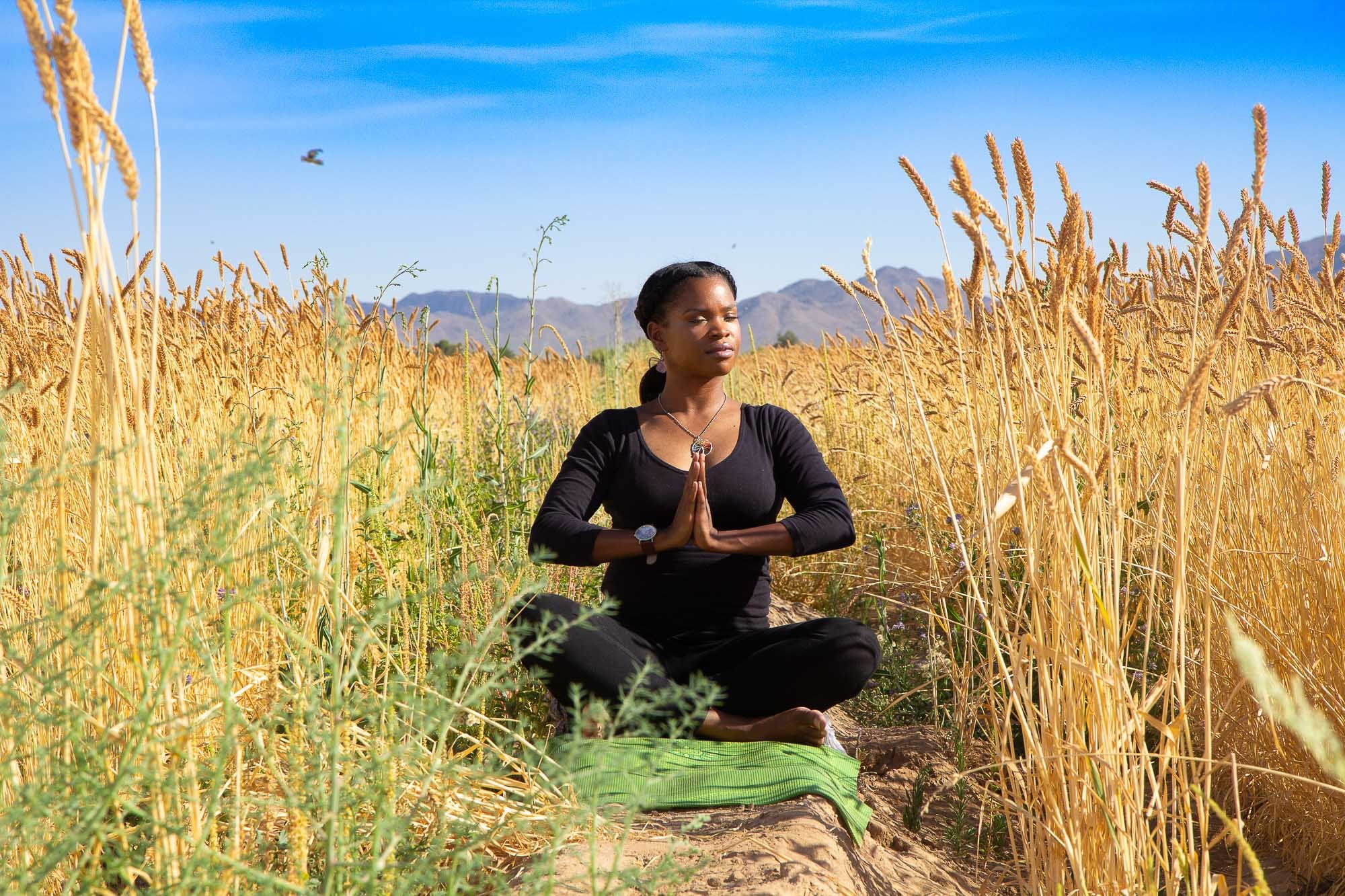 In the serene landscape of Queen Creek, Arizona, Jaquesha, a beautiful fitness and meditation instructor, finds solace and connection in the midst of nature. With legs crossed and palms gently pressed together, she sits in a field brimming with life,