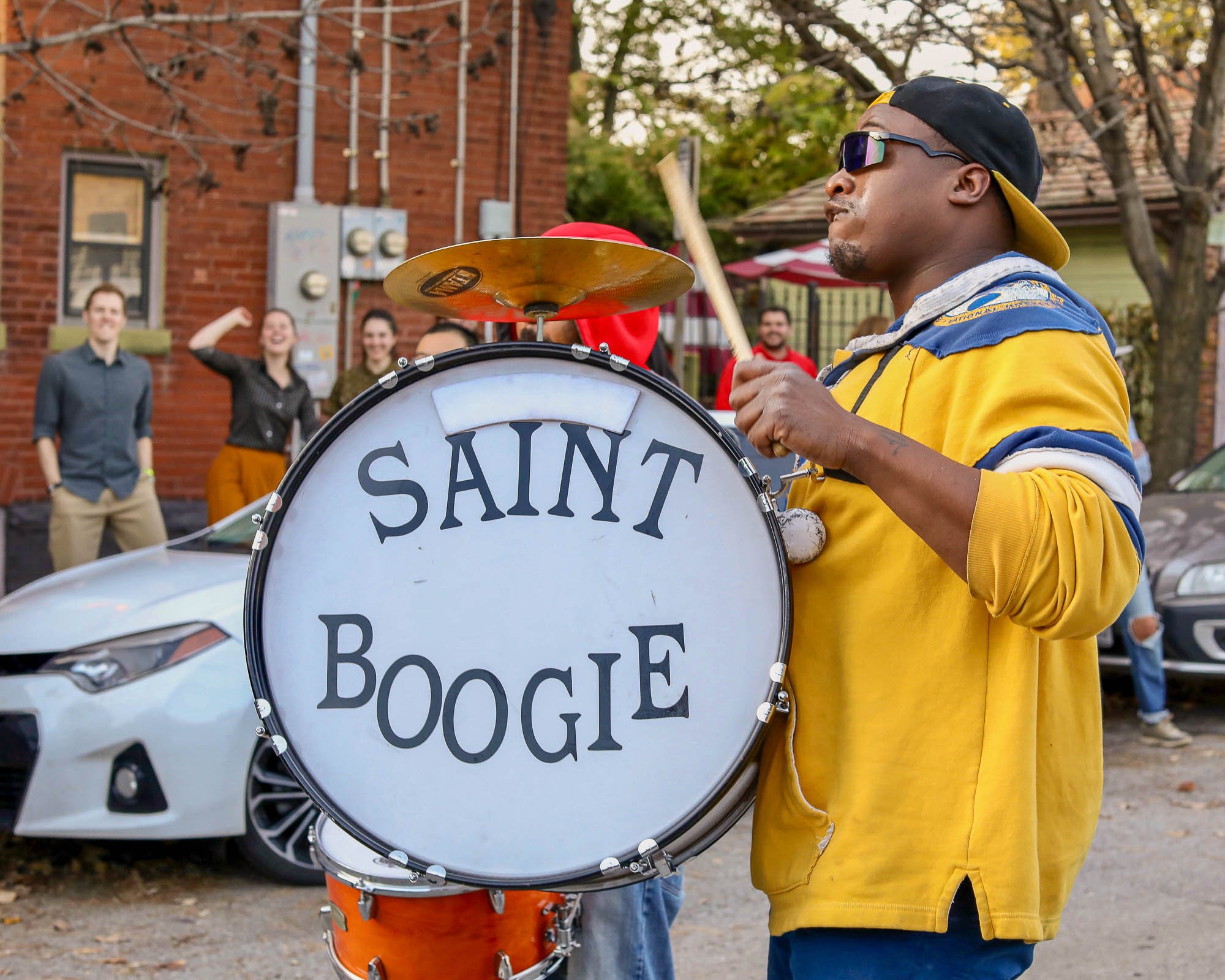 In a spirited outdoor scene on Cherokee Street in St. Louis, Missouri, band member Marvin Bell commands attention as he energetically plays the drum for the Saint Boogie Brass Band during the Cherokee Street Jazz Crawl Parade. Dressed in a striking y