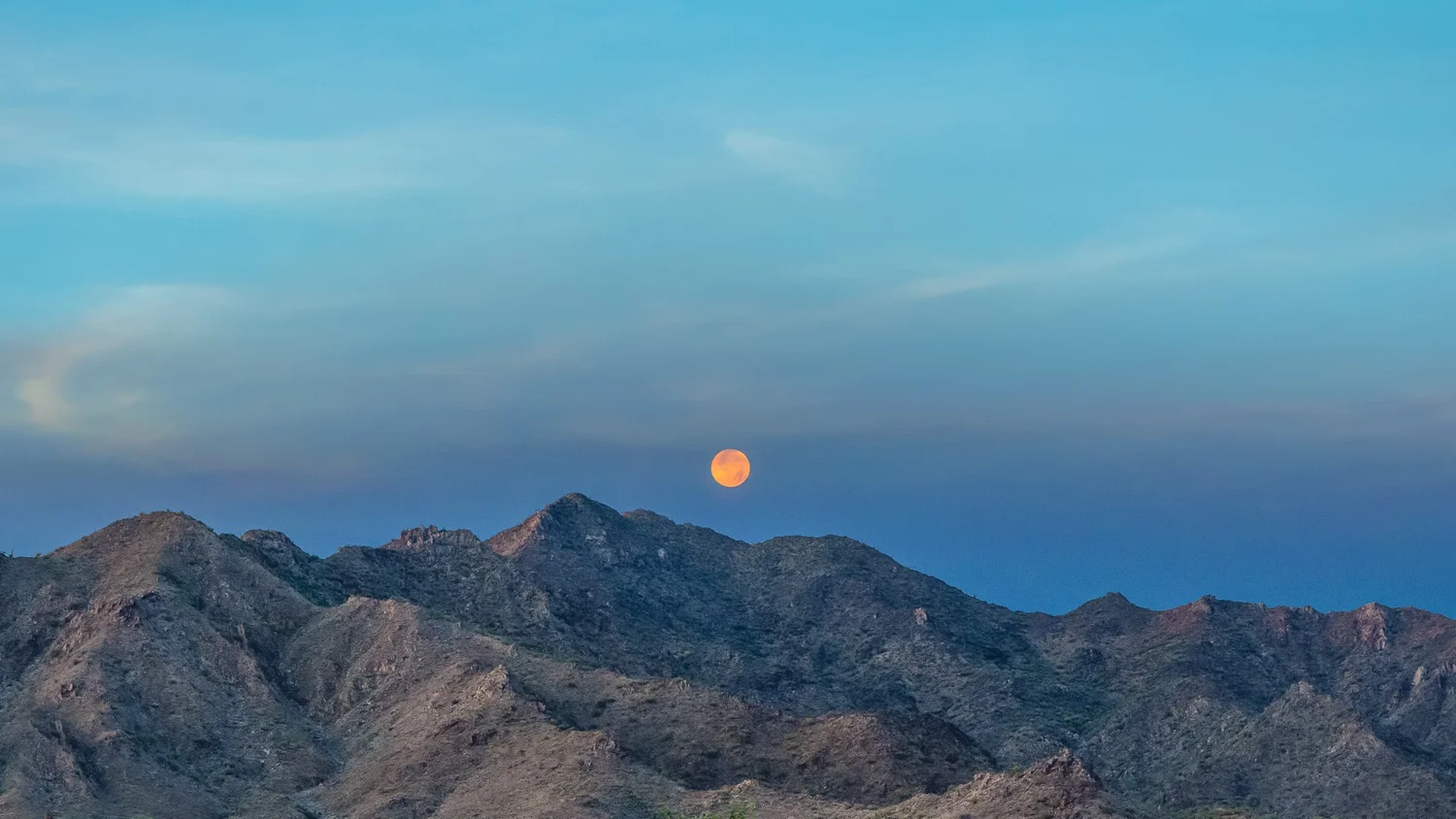 An orange moon rises above the San Tan Mountains in Arizona