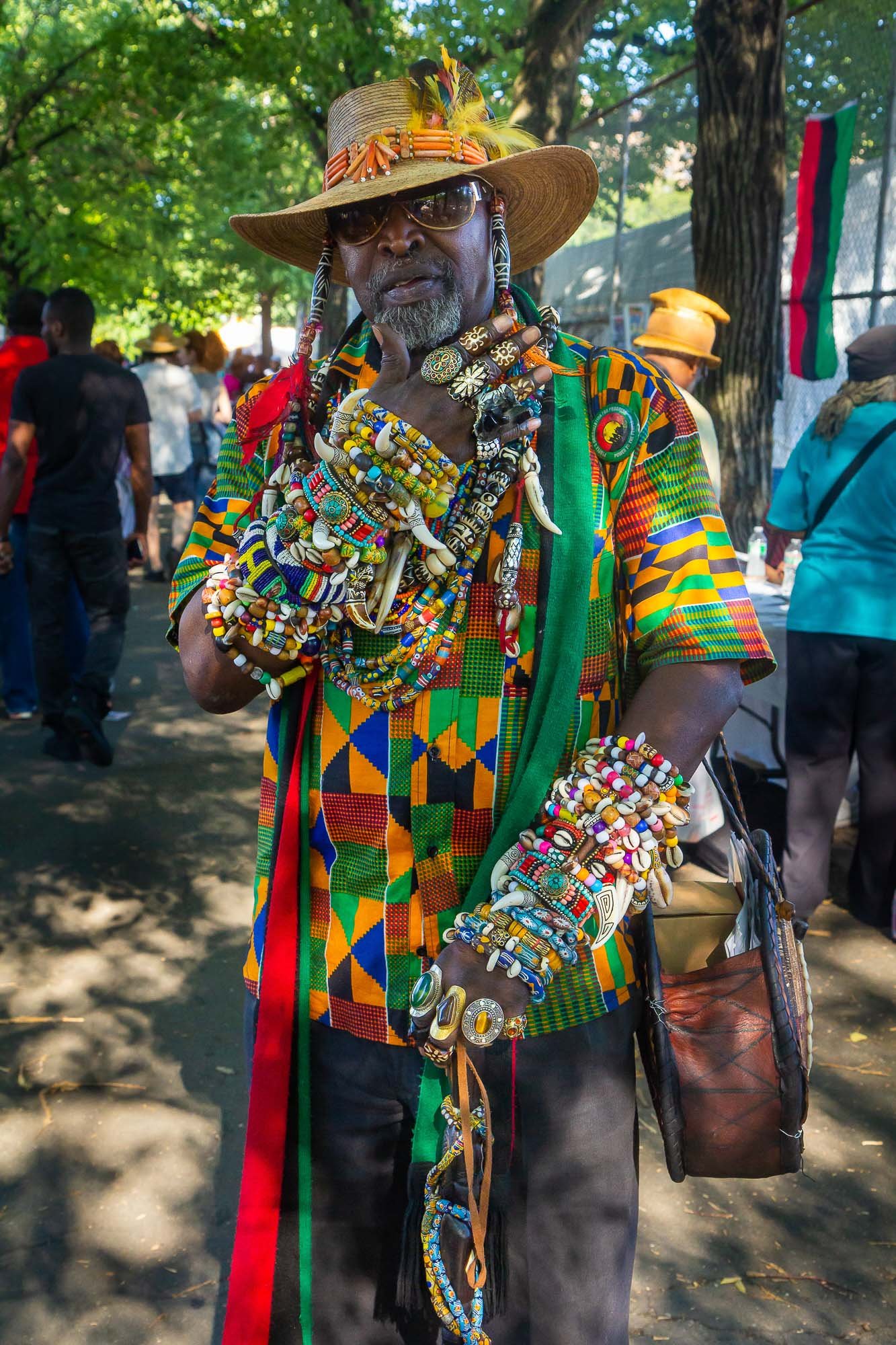 In the lively ambiance at the International African Arts Festival in Brooklyn, a Brooklyn native stands out exquisitely in his culturally inspired and vibrant attire. Adorned with a multitude of colorful beads, necklaces, bracelets, and ornate rings