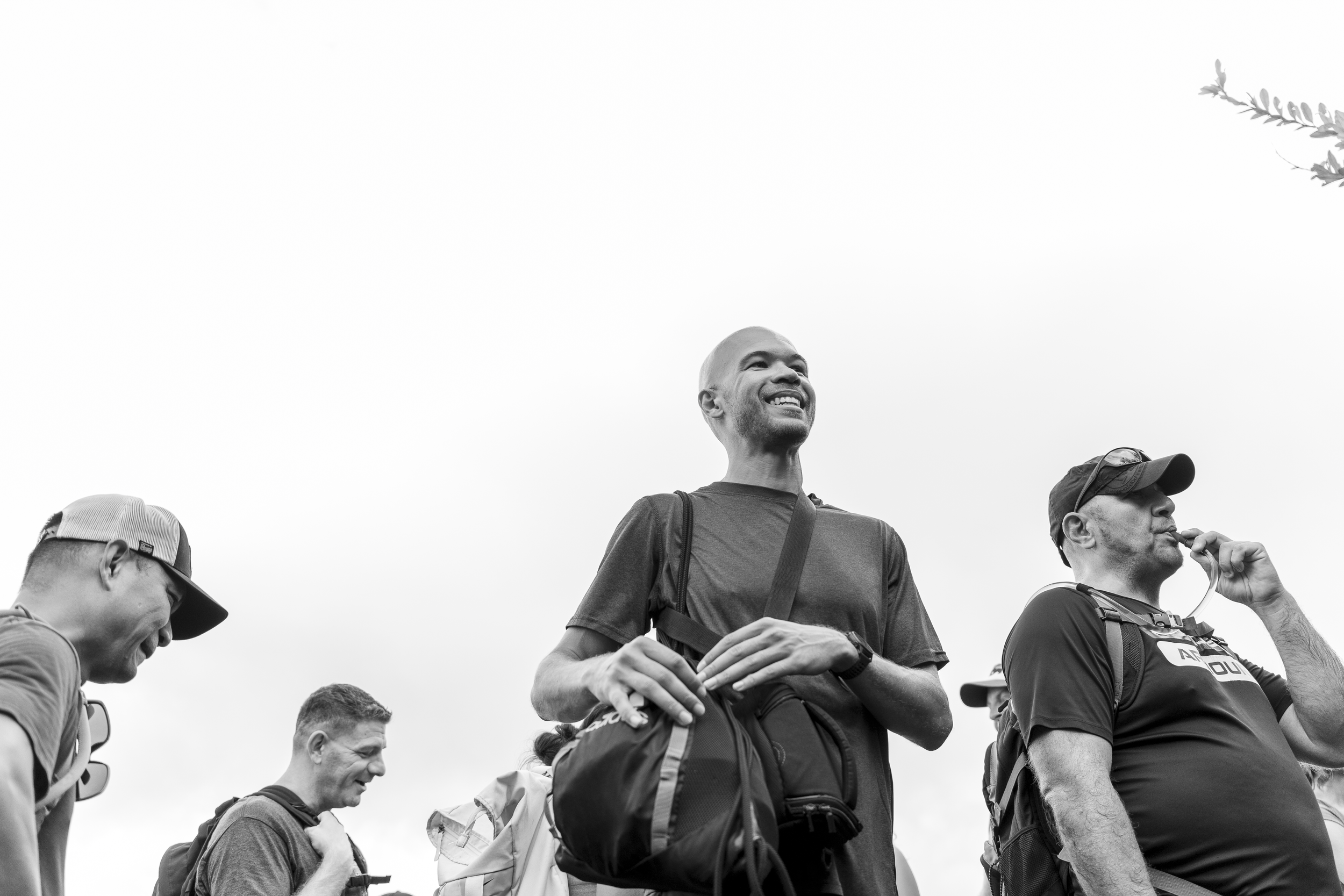 Group of people with backpacks outdoors, smiling and talking, in black and white.