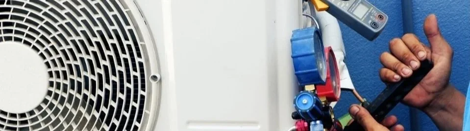A technician servicing an air conditioning unit with tools and gauges.