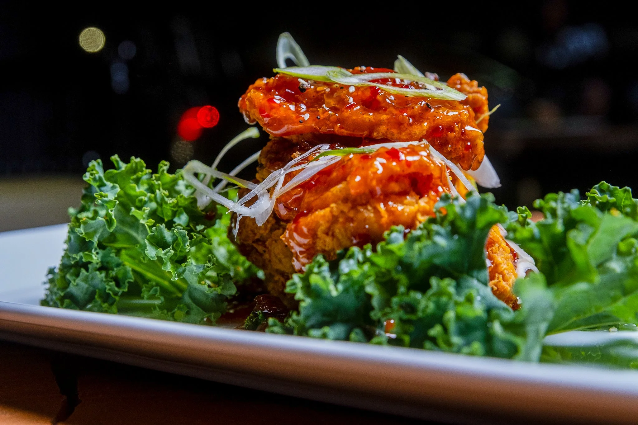 Best professional food photography crispy chicken wings drizzled with spicy sauce topped with sliced green onions on greens on white plate in New York City and shot by Lumumba David from David Media Group