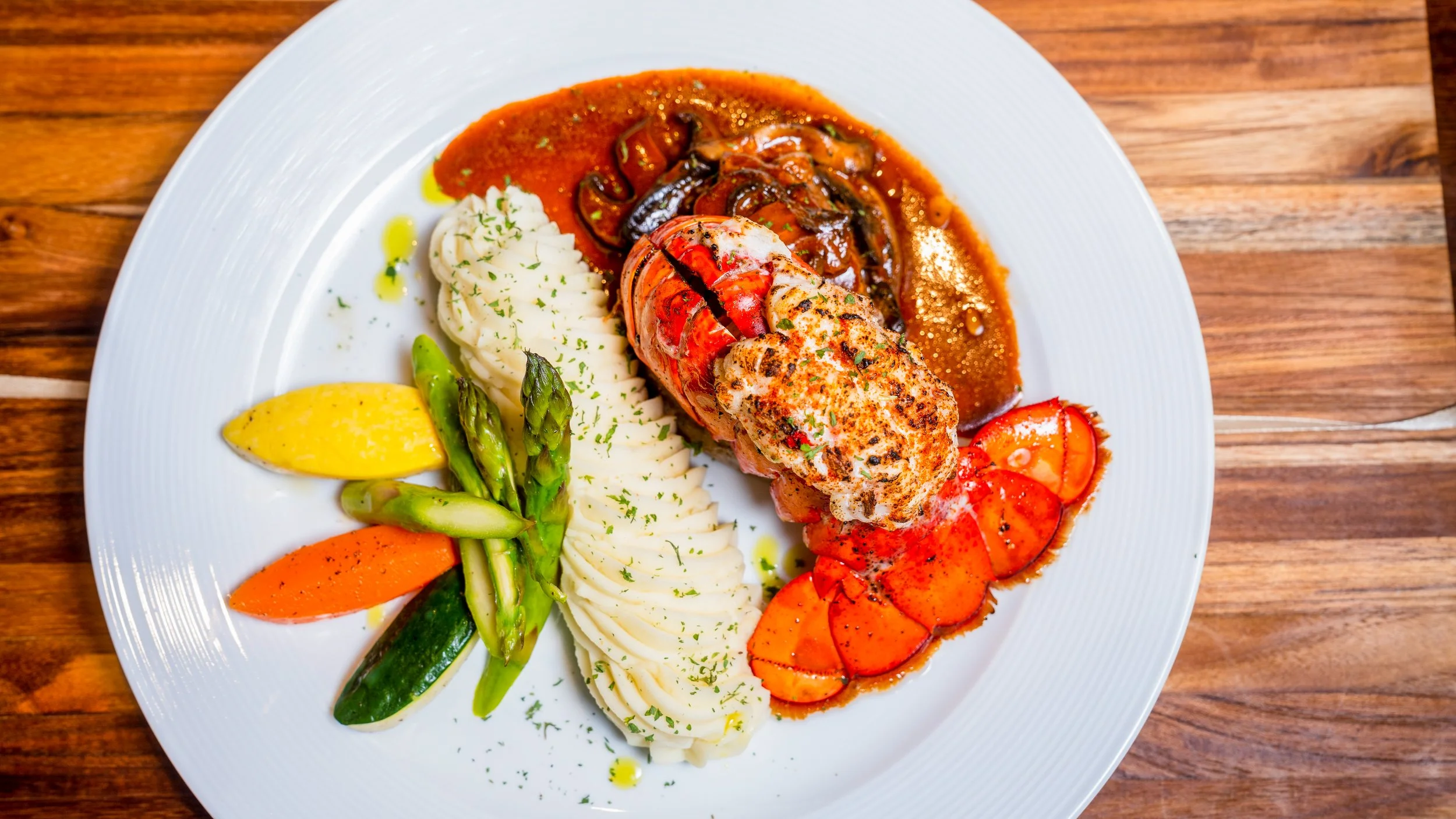 Best restaurant food photography lobster tail with mashed potatoes herb garnish roasted carrots asparagus and cherry tomatoes on wooden table in New York City and shot by Lumumba David from David Media Group