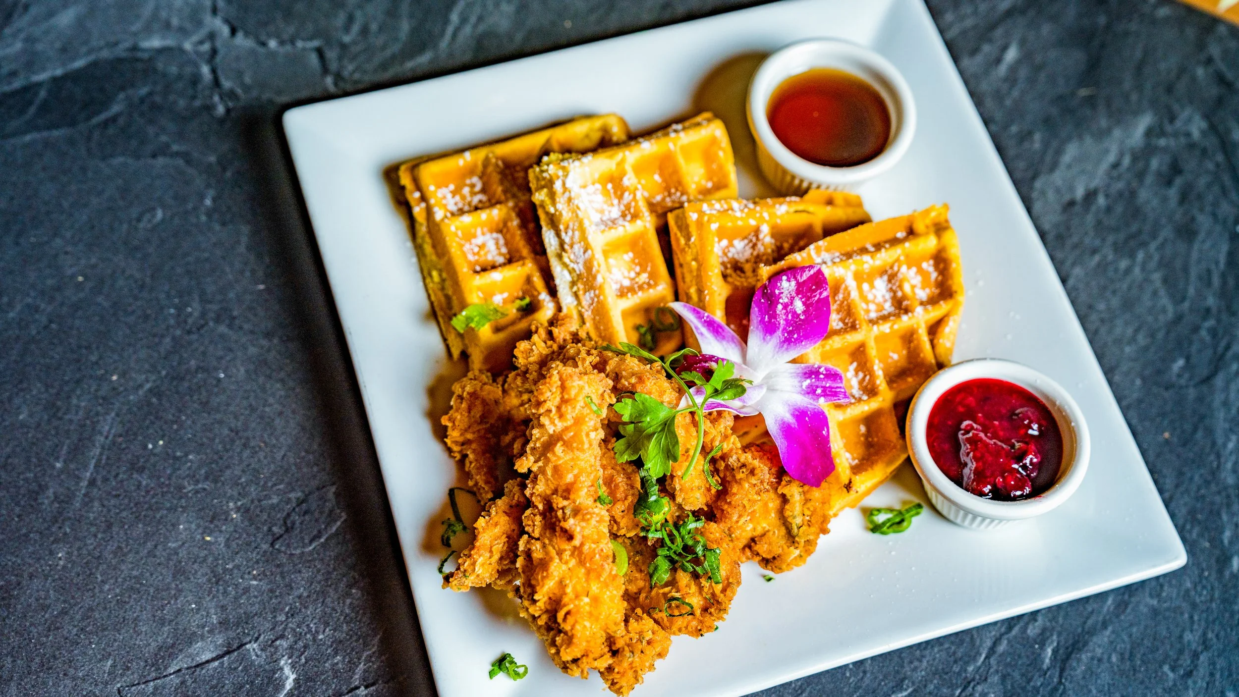 Best food and beverage photography chicken tenders and waffles with powdered sugar orchid green herbs syrup and berry jam on white square plate in New York City and shot by Lumumba David from David Media Group