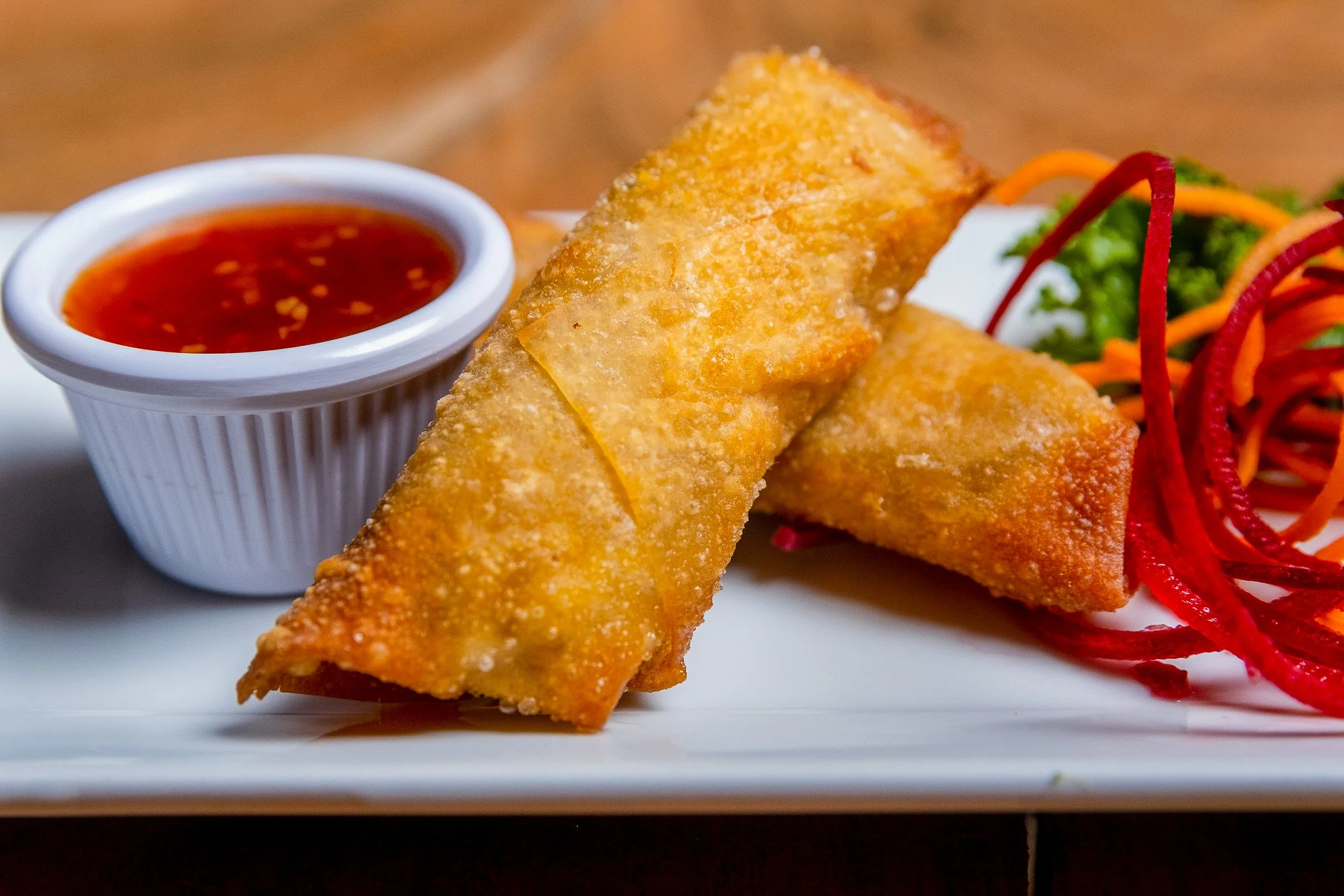 Best brand food photography crispy spring rolls plated with red dipping sauce and small salad shredded carrots red peppers greens in New York City and shot by Lumumba David from David Media Group