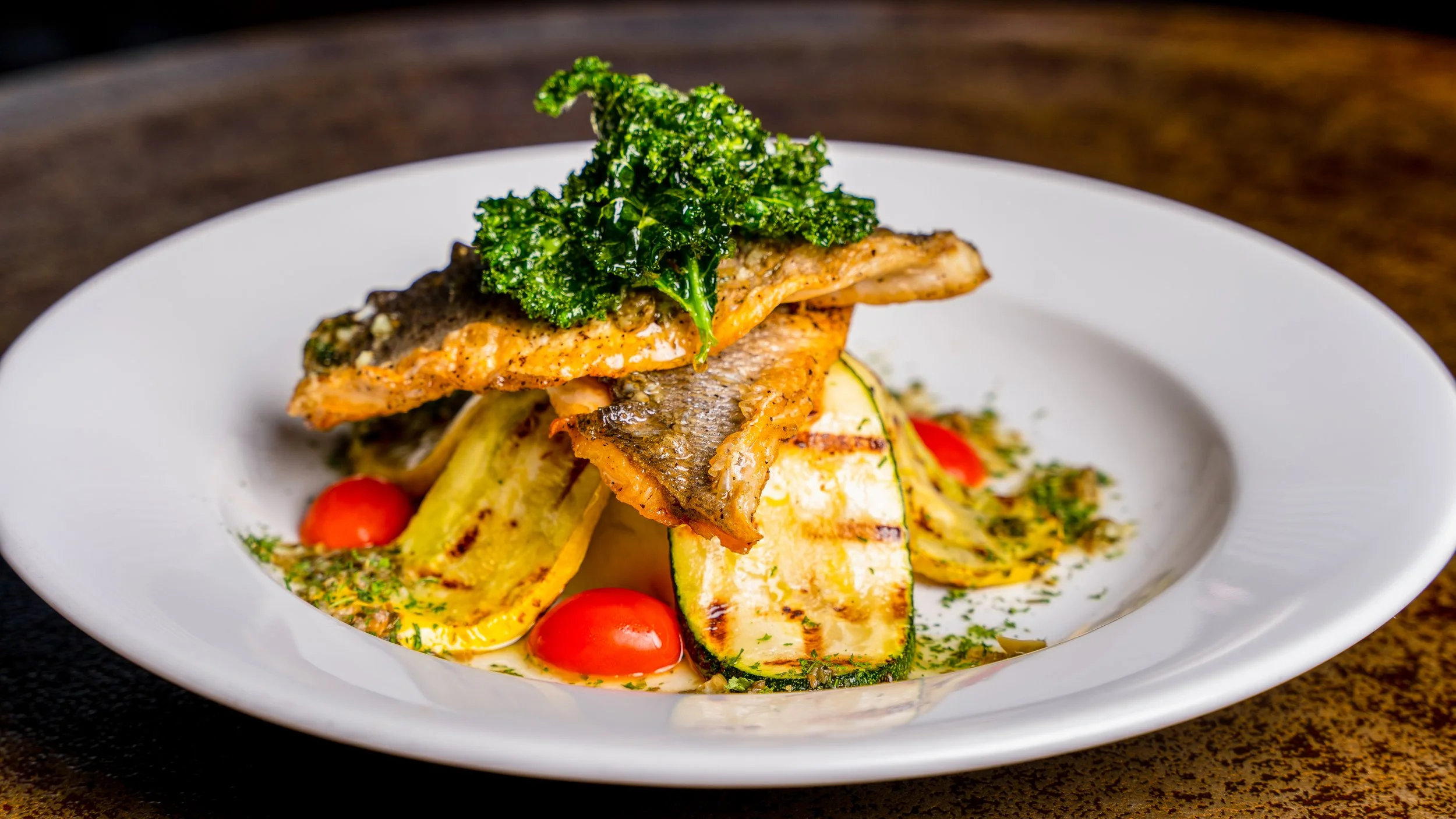 Best restaurant food photography grilled fish with lemon slices grilled zucchini cherry tomatoes side greens and herb garnish on plate in New York City and shot by Lumumba David from David Media Group