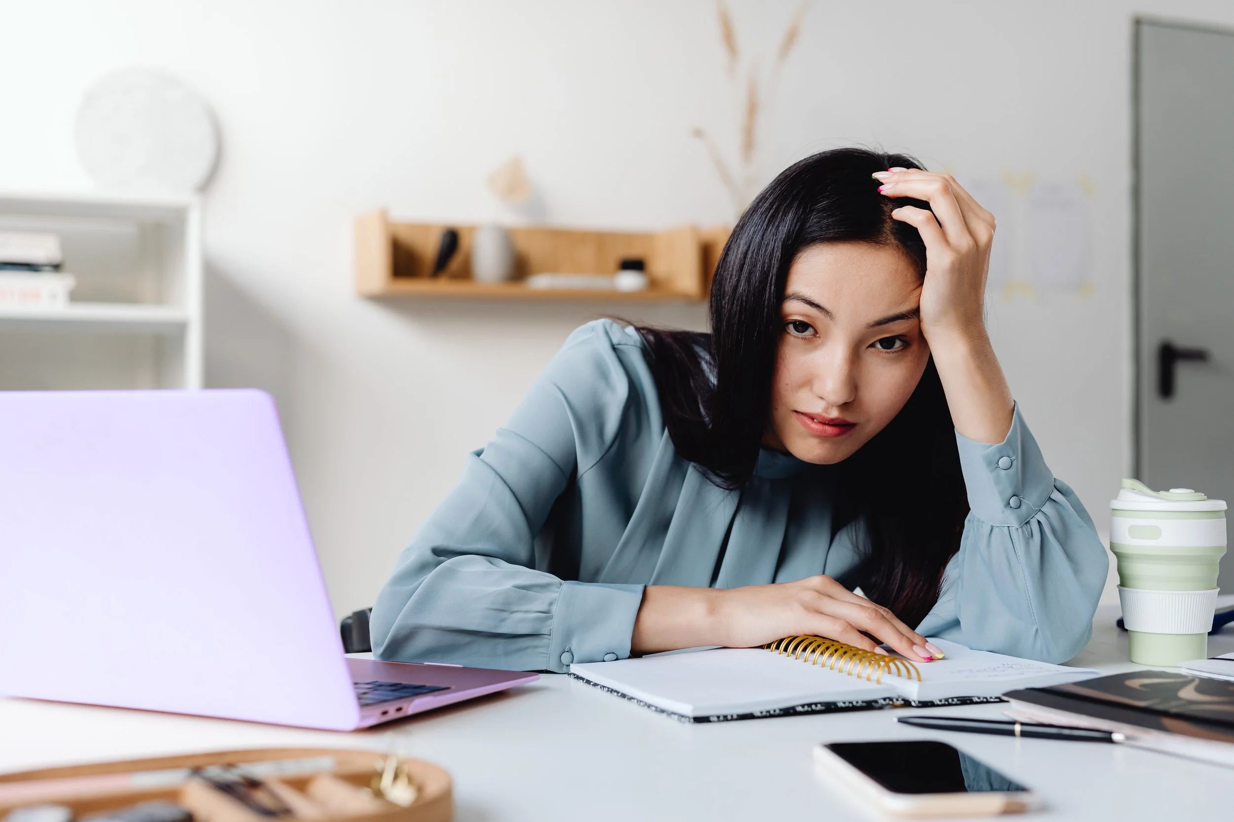 Image of young Asian woman sitting at her desk looking tired and maybe a little frustrated.