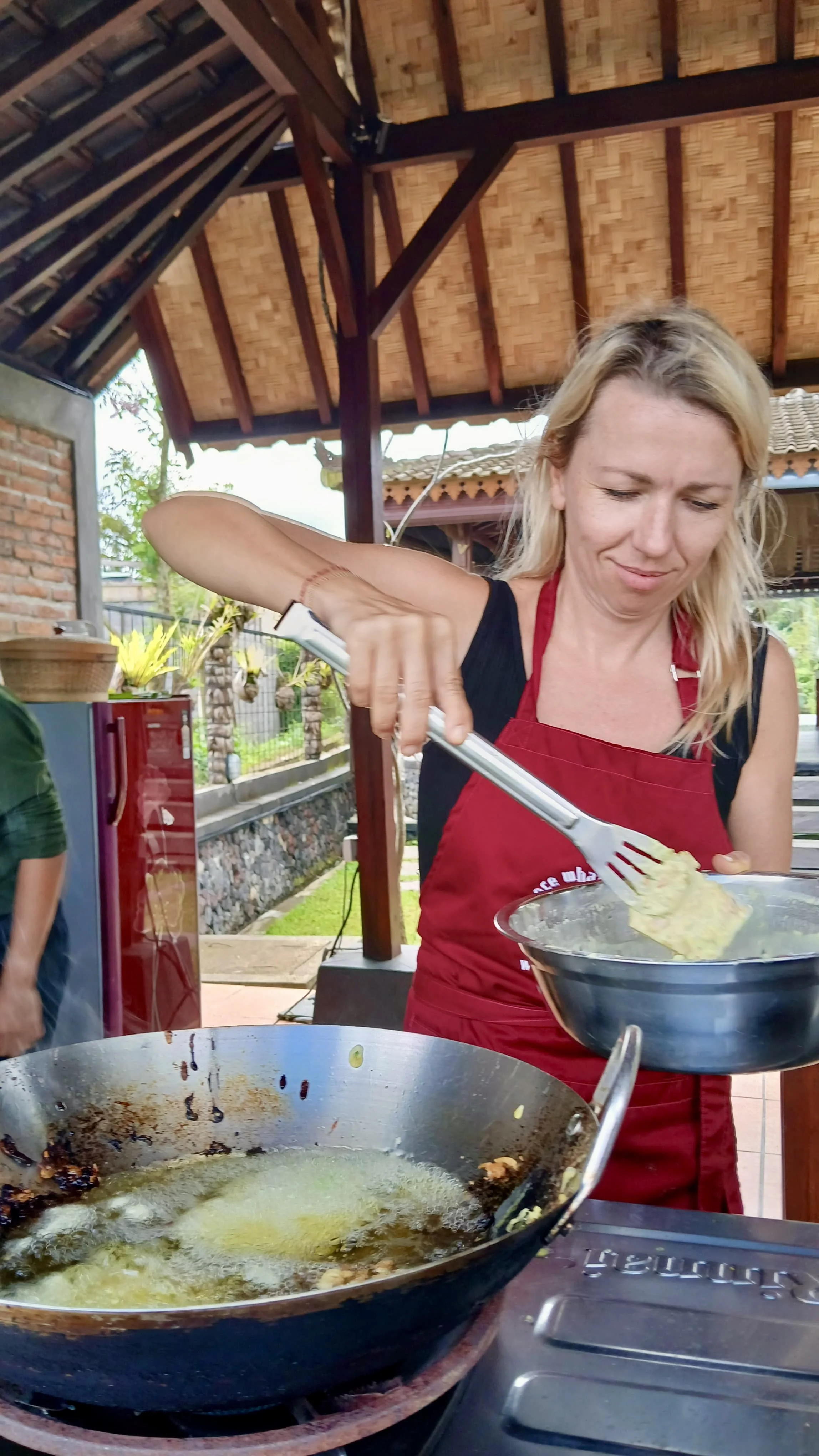 Woman in a red apron cooking food in a large wok outdoors.