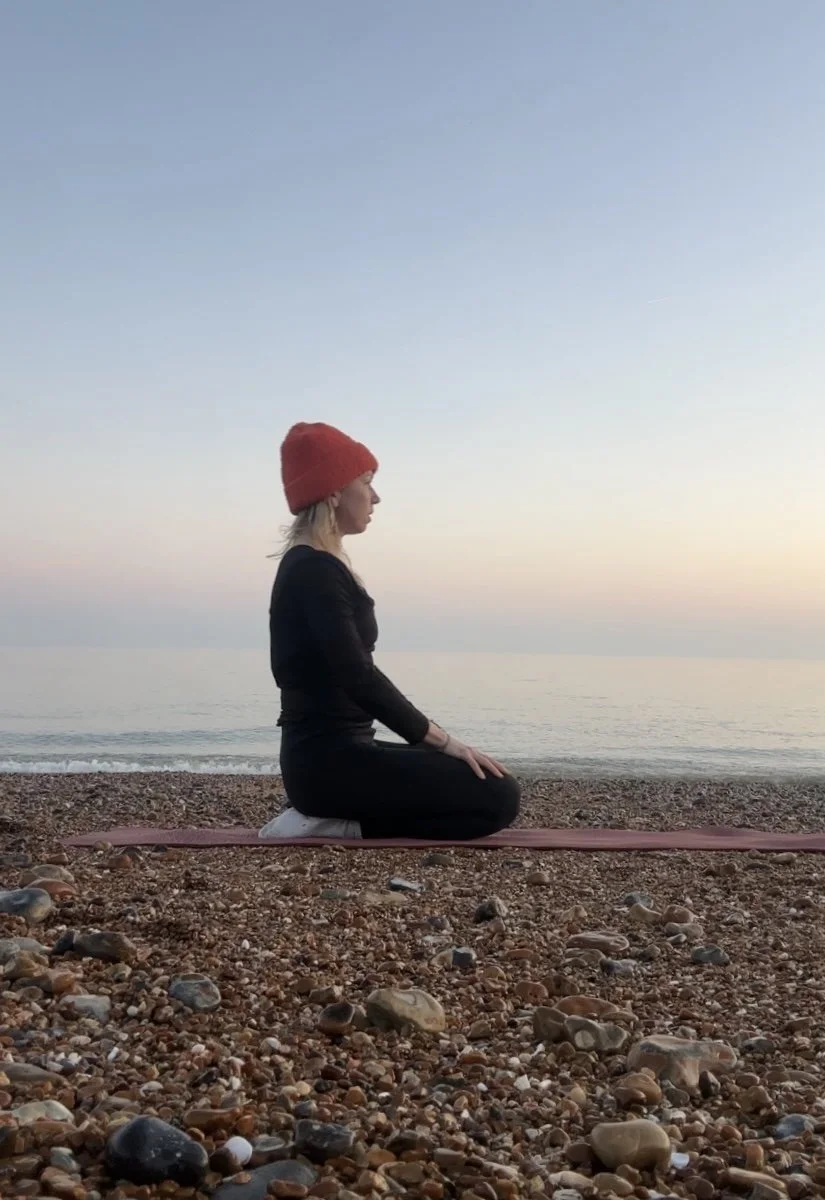 Person meditating on a pebble beach at sunrise
