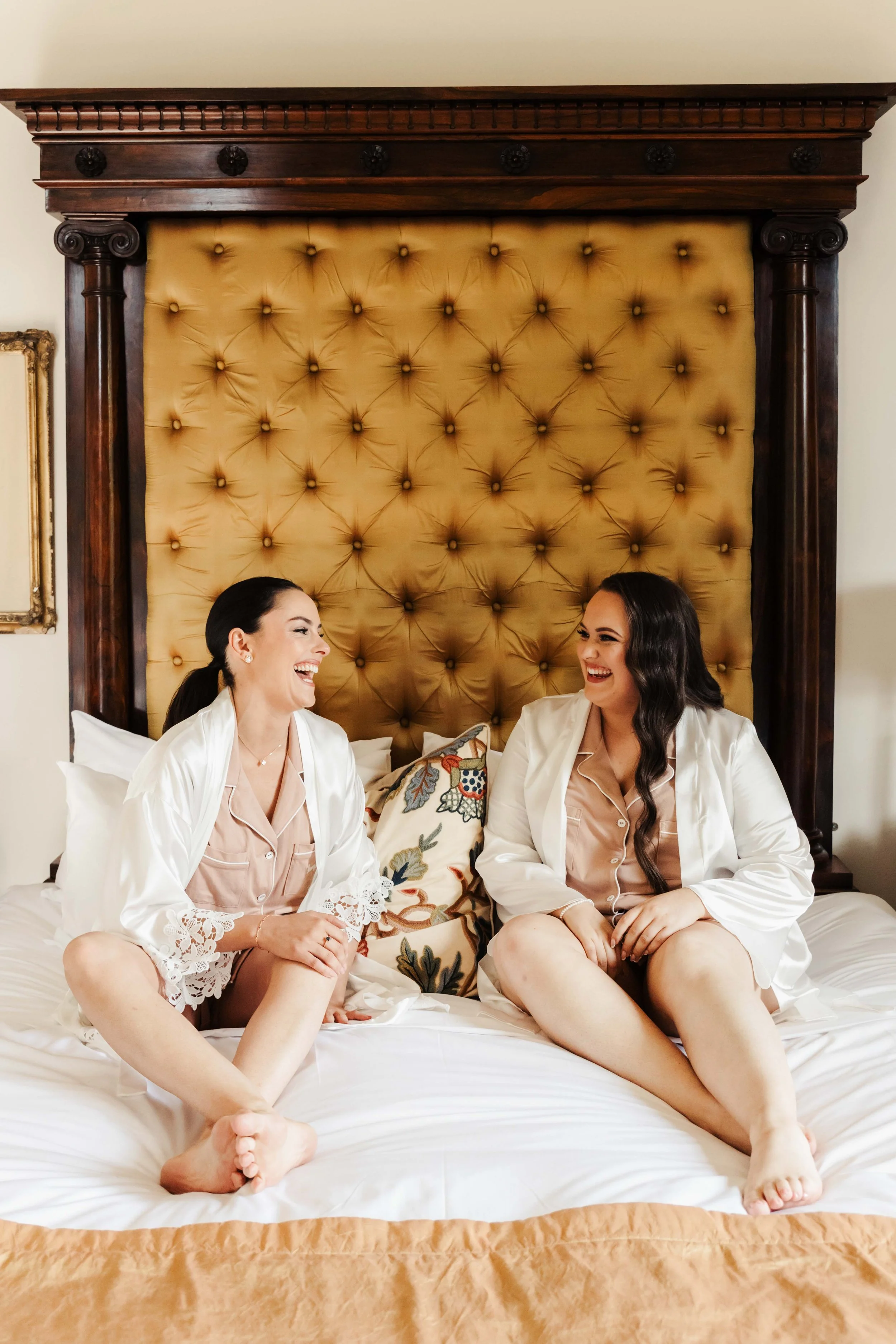 Wedding photography of a wedding in Hobart, Tasmania. Bride and bridesmaid sit happy and laughing on a bed