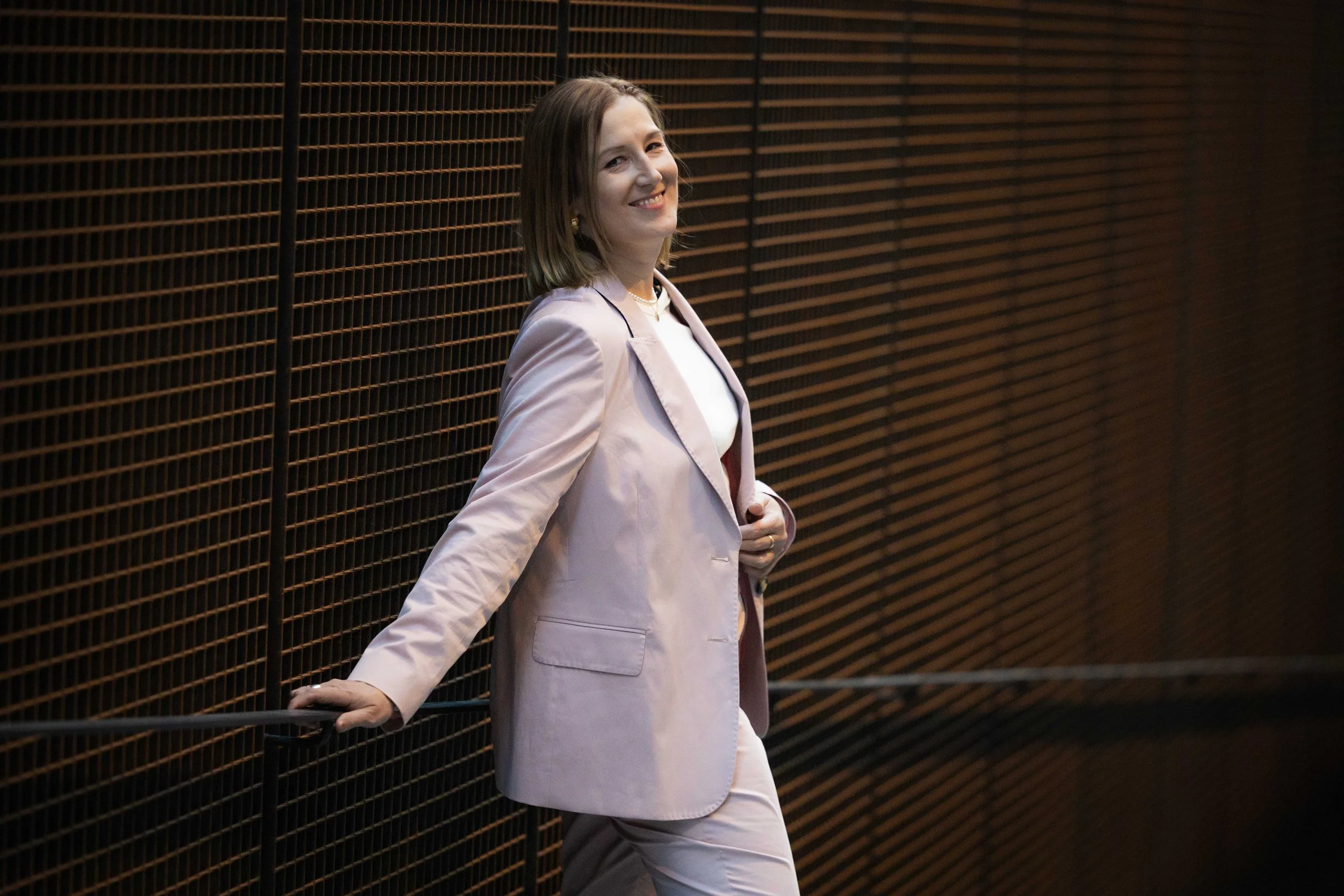 Nuori nainen hymyilee, seisoo metallilistalla seinän edessä.