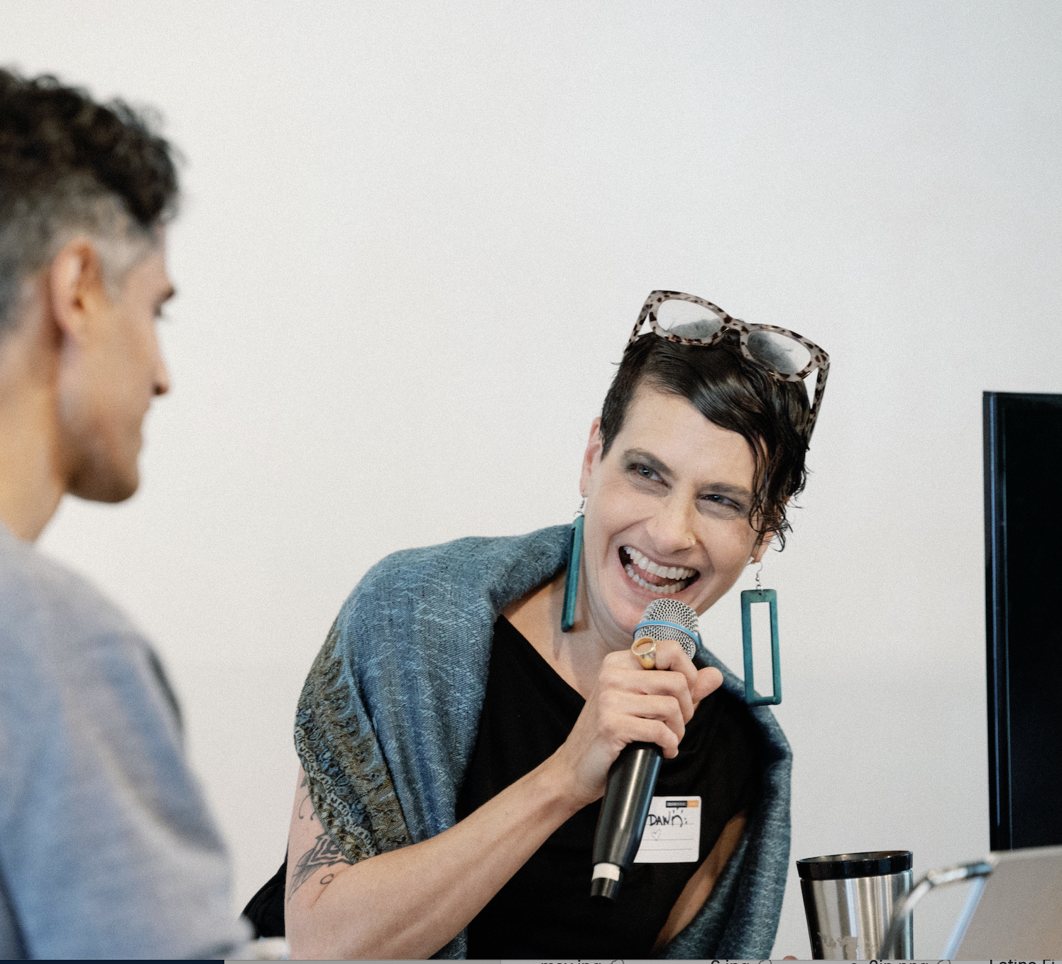Dawn in a sleeveless black top, a turquoise wrap, and long turquoise earring, laughing, holding a microphone