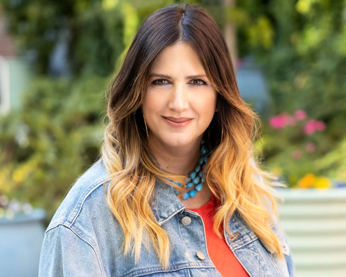 Jessica Schmoll smiling in denim jacket and orange shirt with turquoise necklace