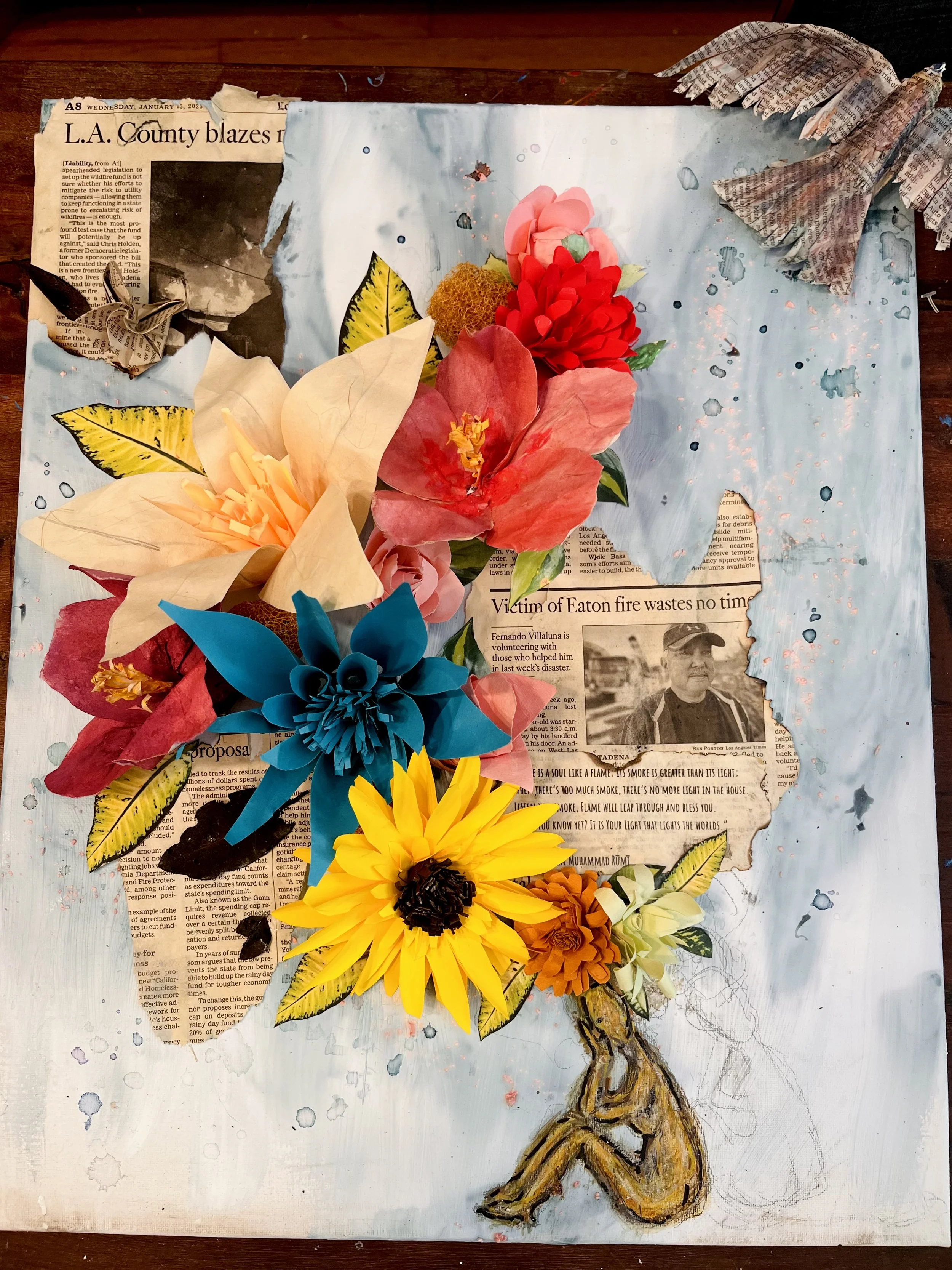 Mixed media artwork featuring paper flowers in various colors arranged around torn newspaper clippings, with a painted background and a sketched figure of a person sitting with their head resting on their knees.