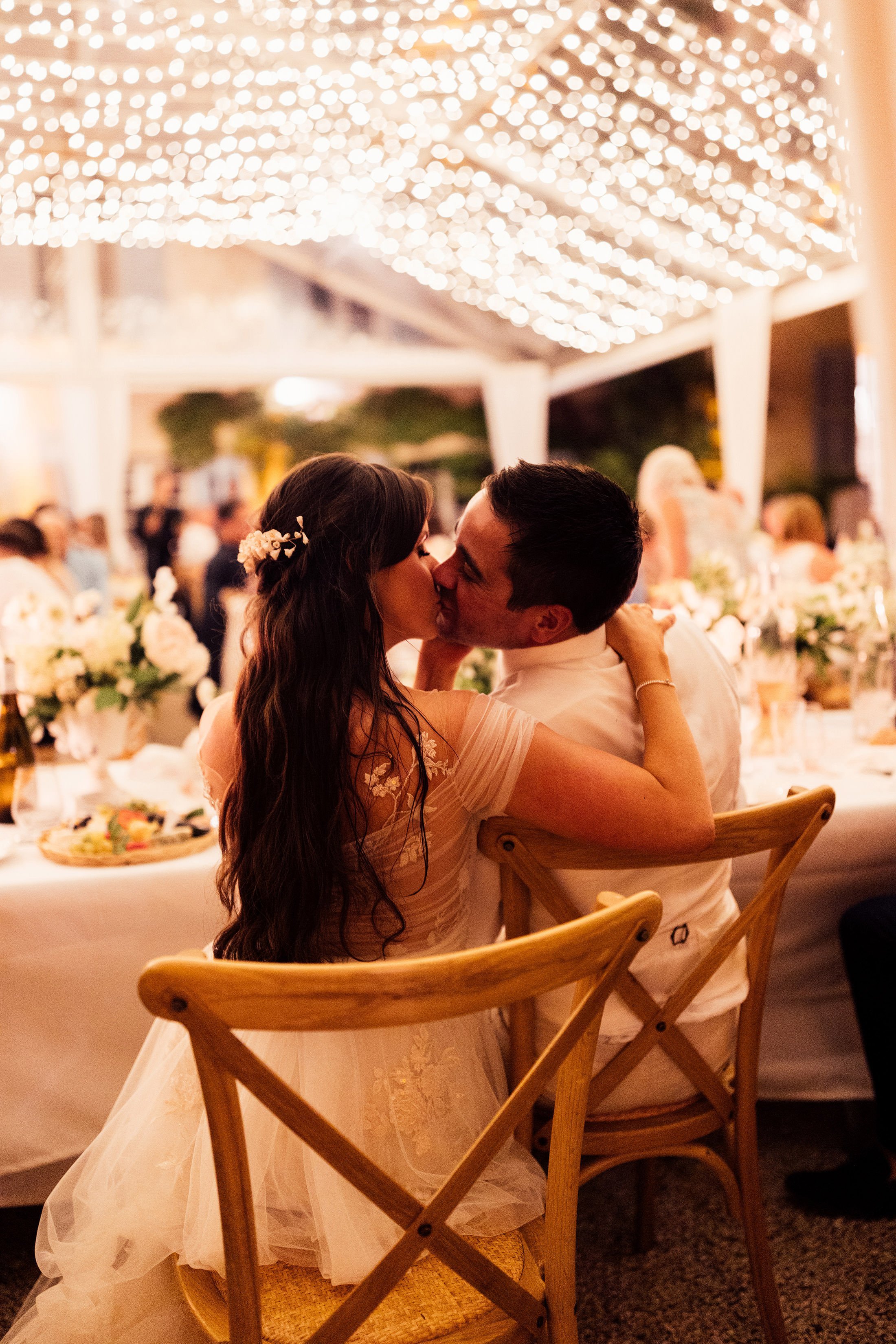 couple kiss during wedding reception with string lights above