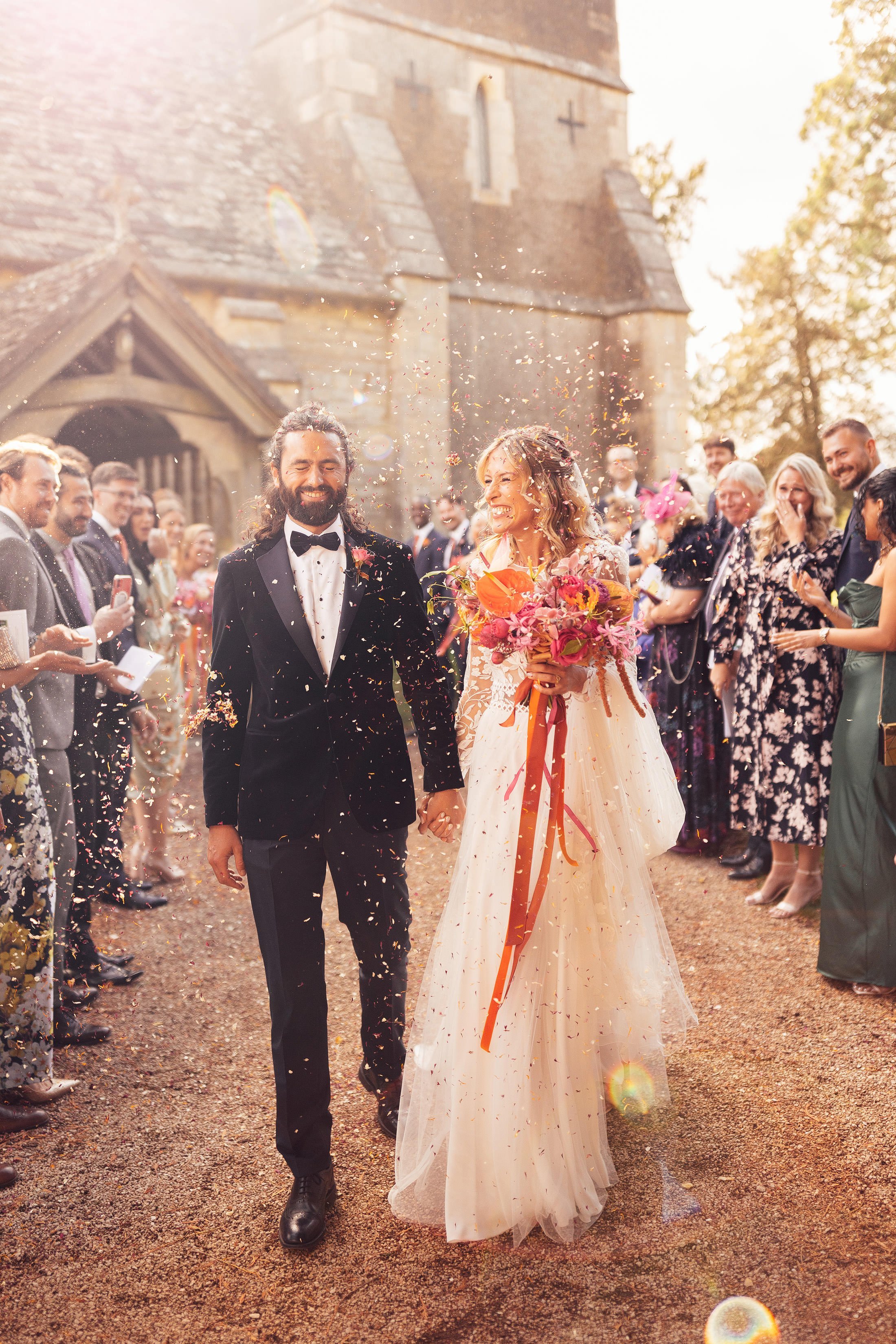 groom with long hair and bride in margaux tardits dress confetti moment outside Elmore church