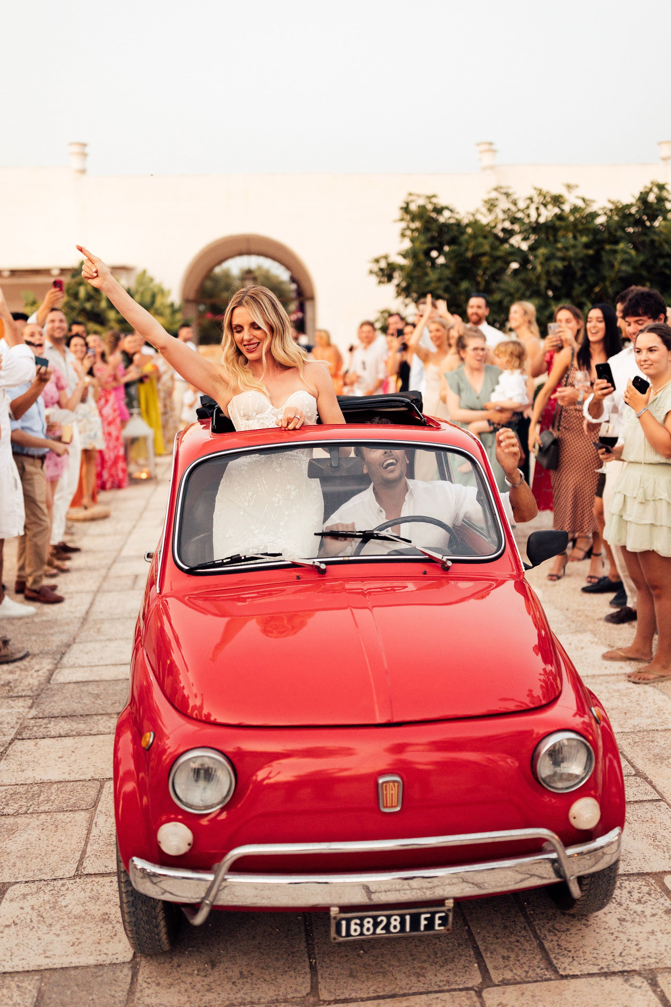bride and groom enter wedding reception in vintage red fiat in Puglia wedding venue