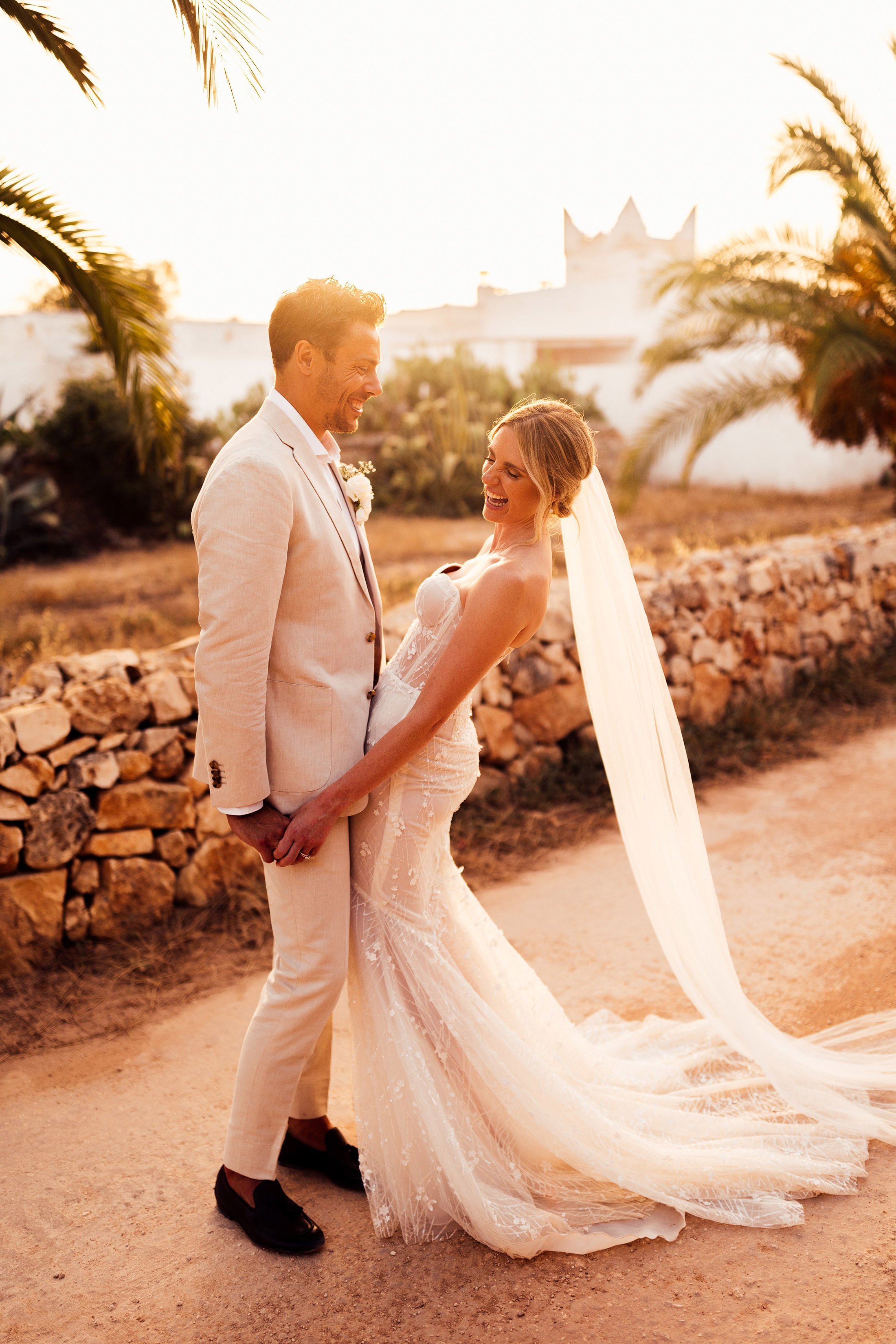 couple embrace at sunset with groom in cream linen suit and bride in galia lahav dress
