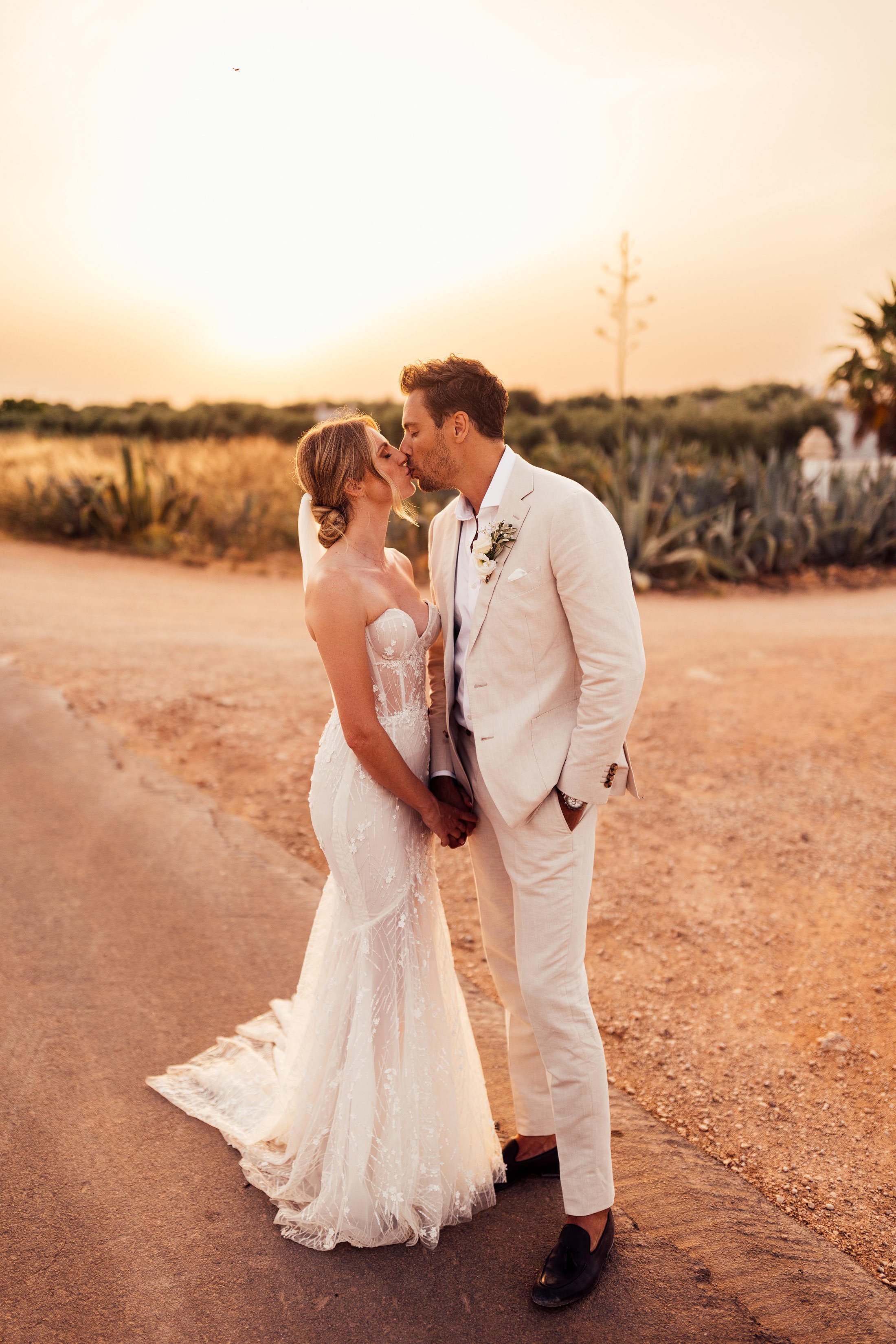 bride in galia lahav dress and groom in cream linen suit kiss at sunset infront of masseria potenti entrance