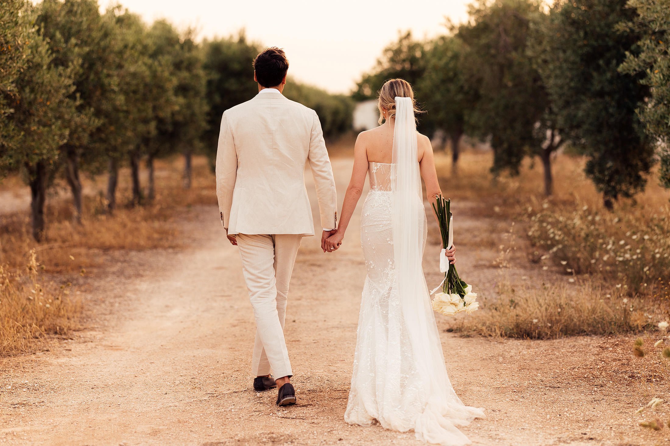 couple walk in olive grove with bride in galia lahav dress