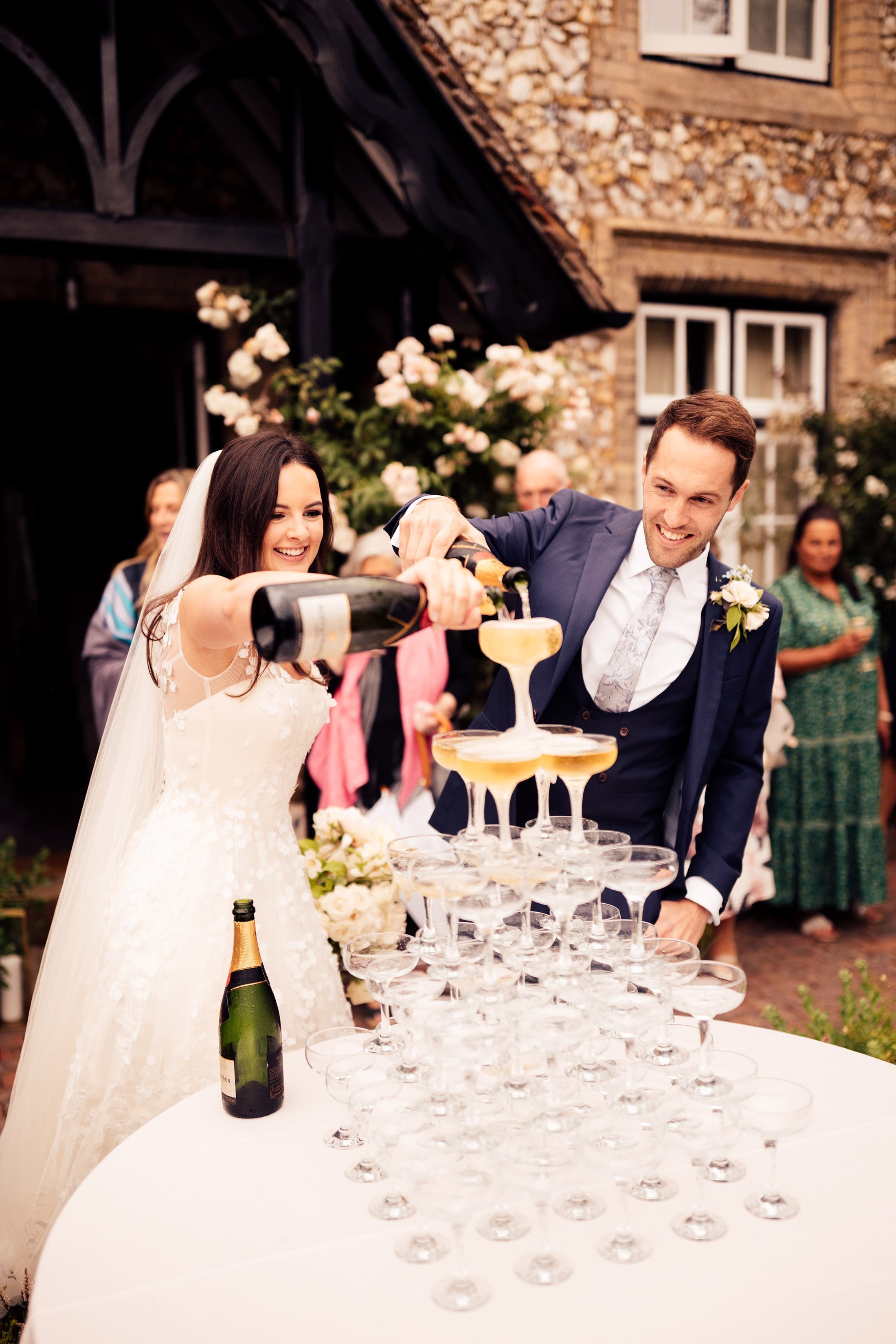 bride in phillipa Lepley dress and groom in blue suit pour champagne tower