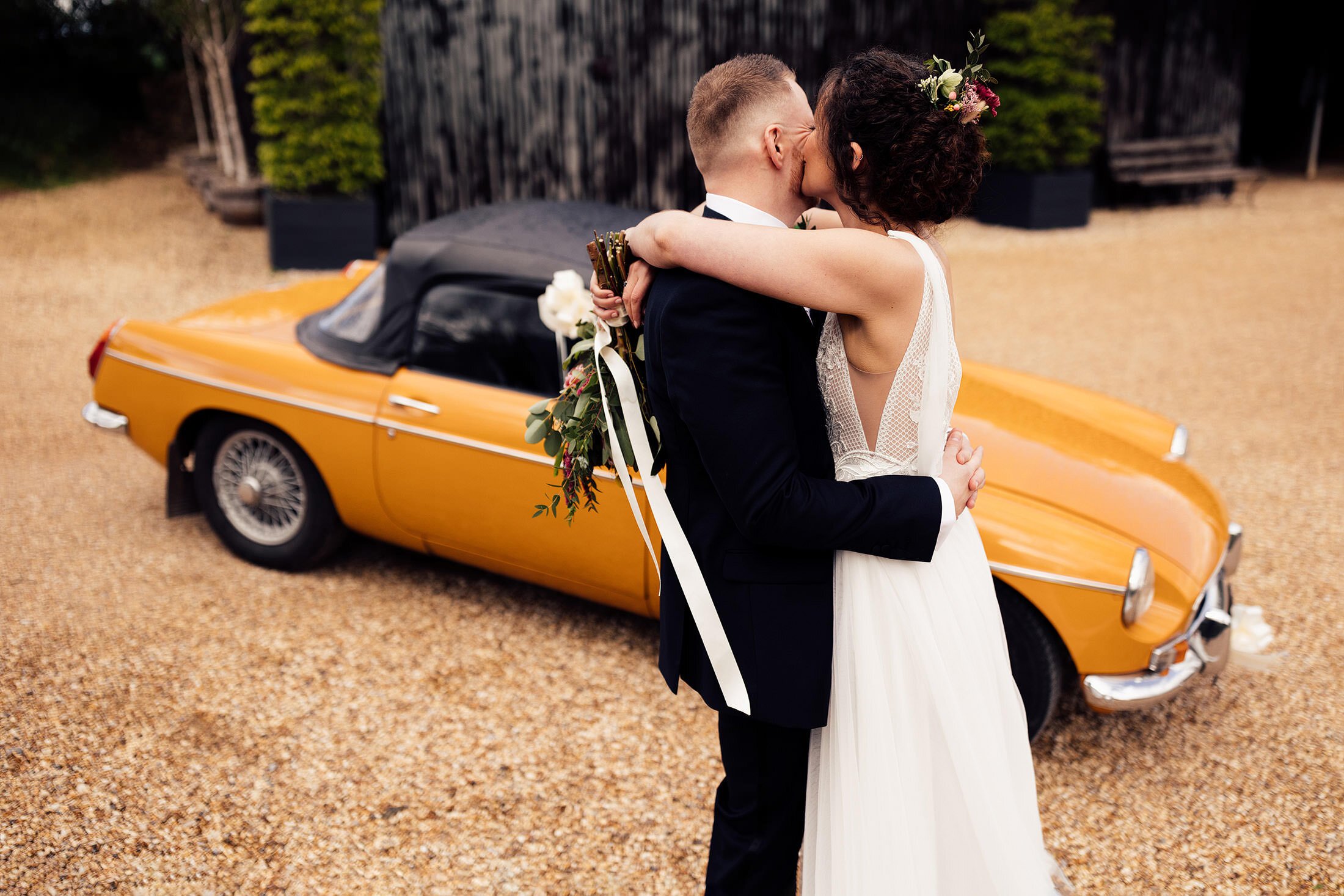 couple embrace in front of vintage car outside Cripps barn