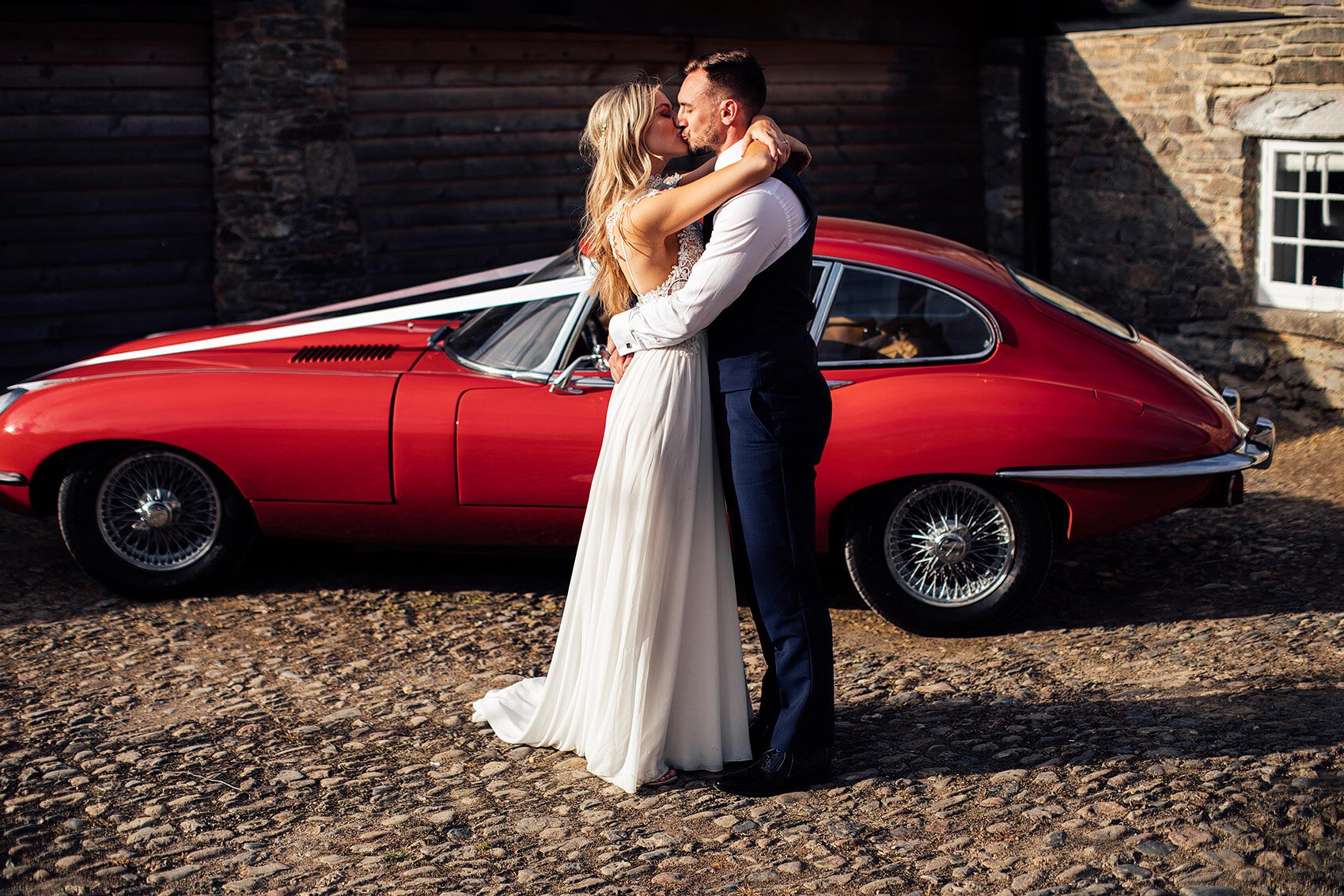 Bride and groom embracing in front of a red sports car