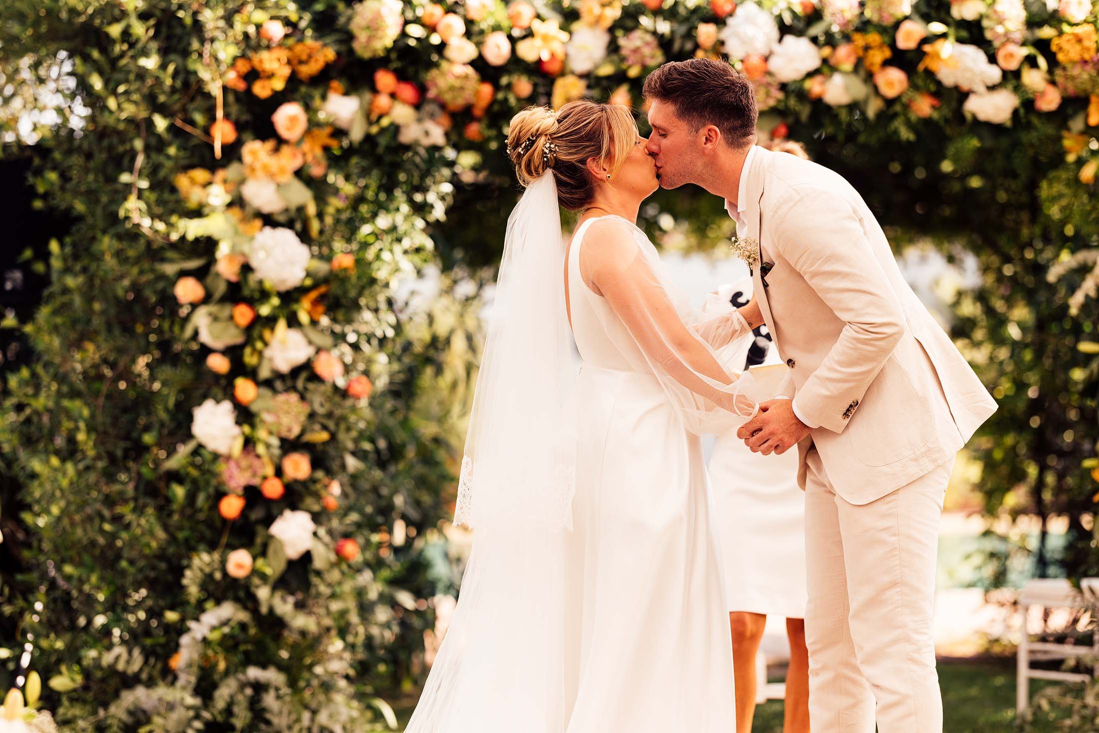 couple share first kiss next to colourful flower arch at spain wedding