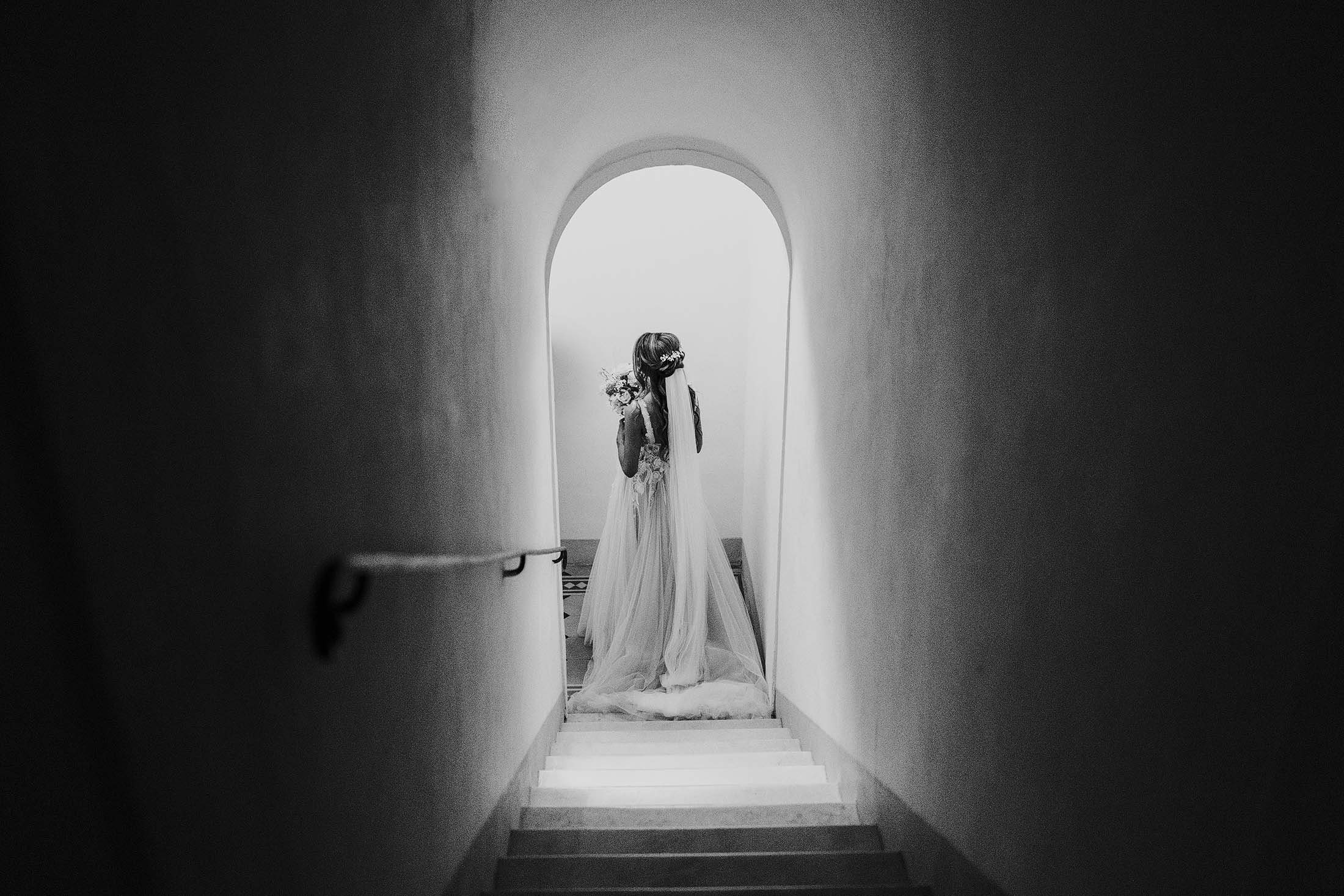 black and white photo of bride walking downstairs to ceremony in Muse by Berta dress