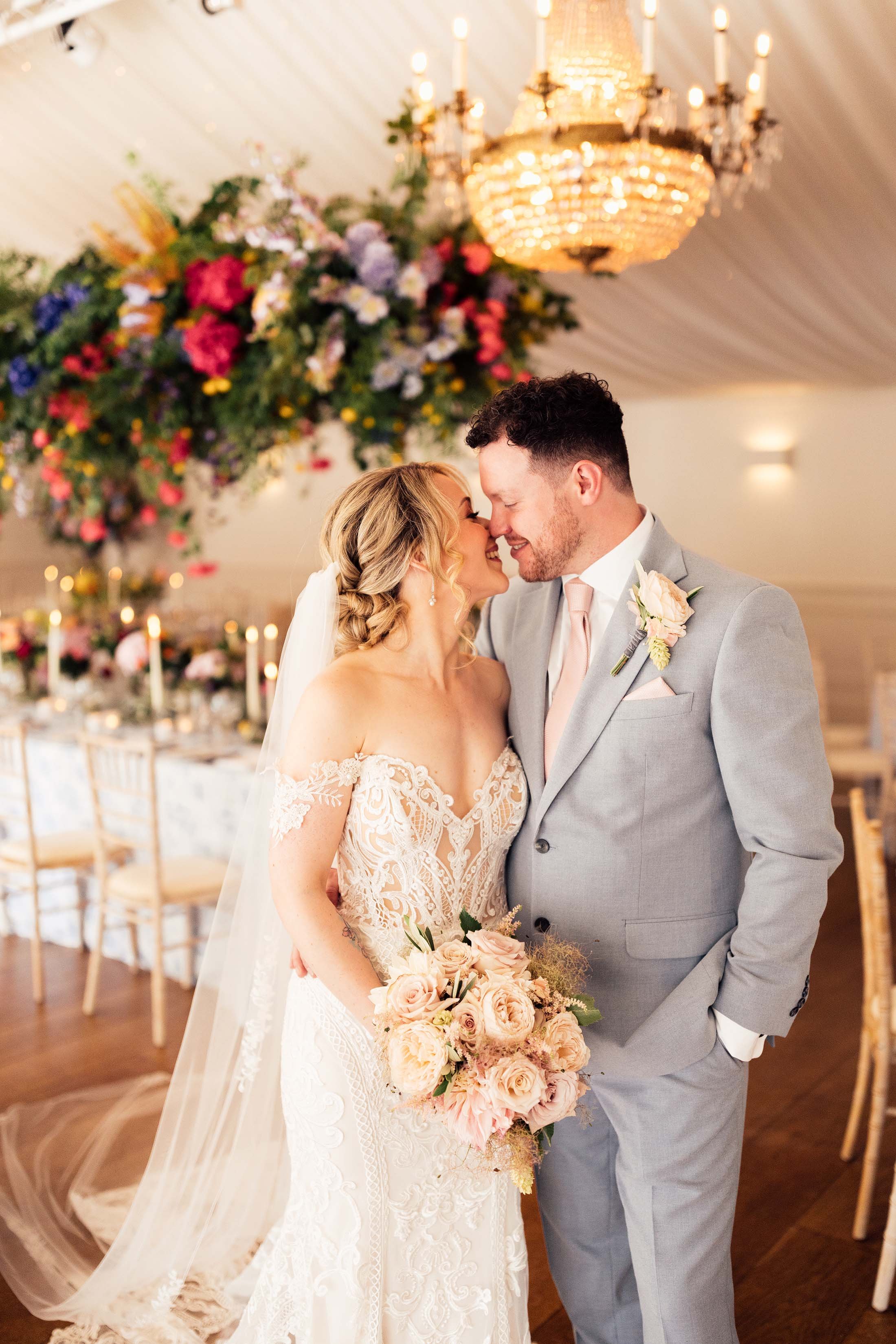 bride and groom kiss in colourful marquee with chandelier installation