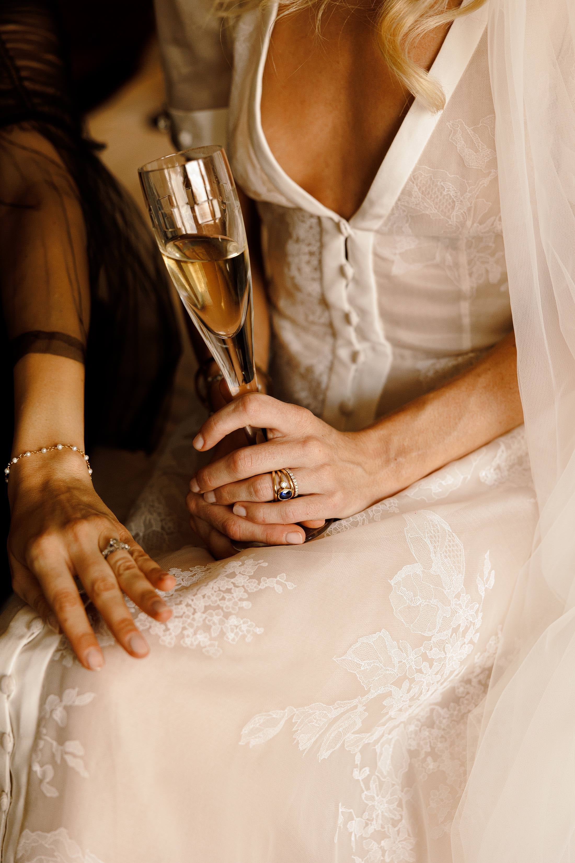 bride holds champagne with close up of vintage jewellery