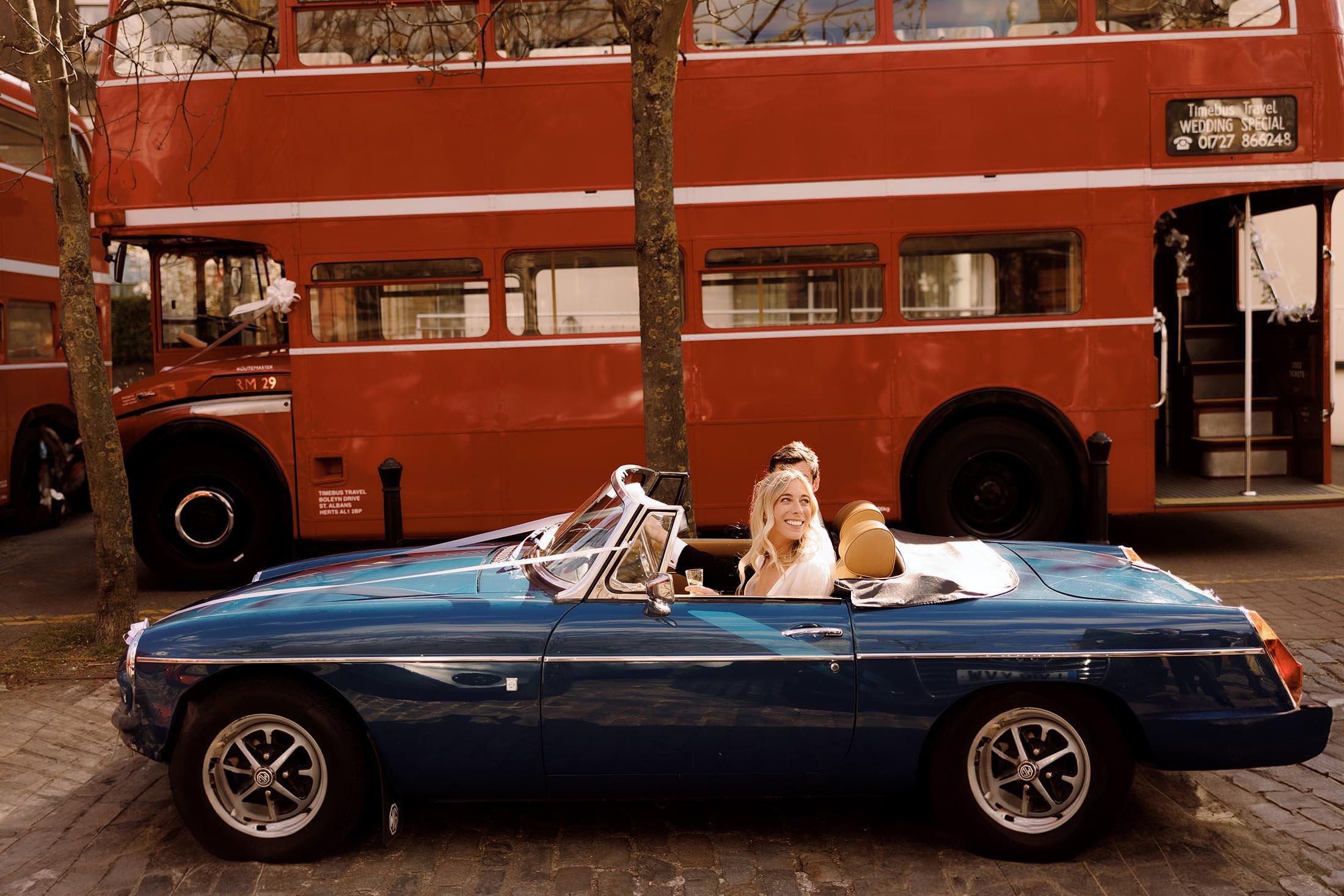 couple drive vintage blue MG through london