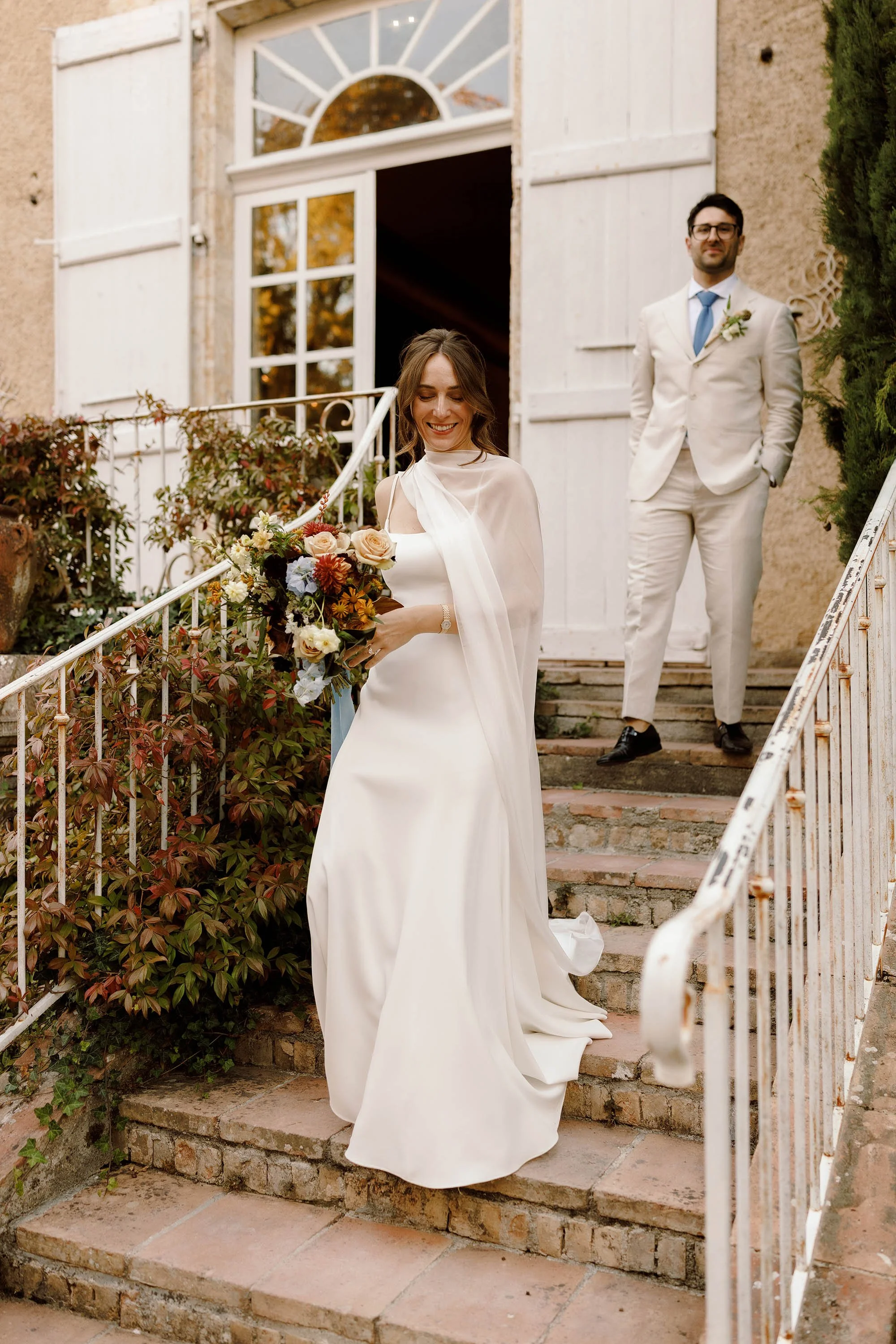 bride in jenny yoo wedding dress with cape walks to see tables at chateau de lartigolle france wedding venue