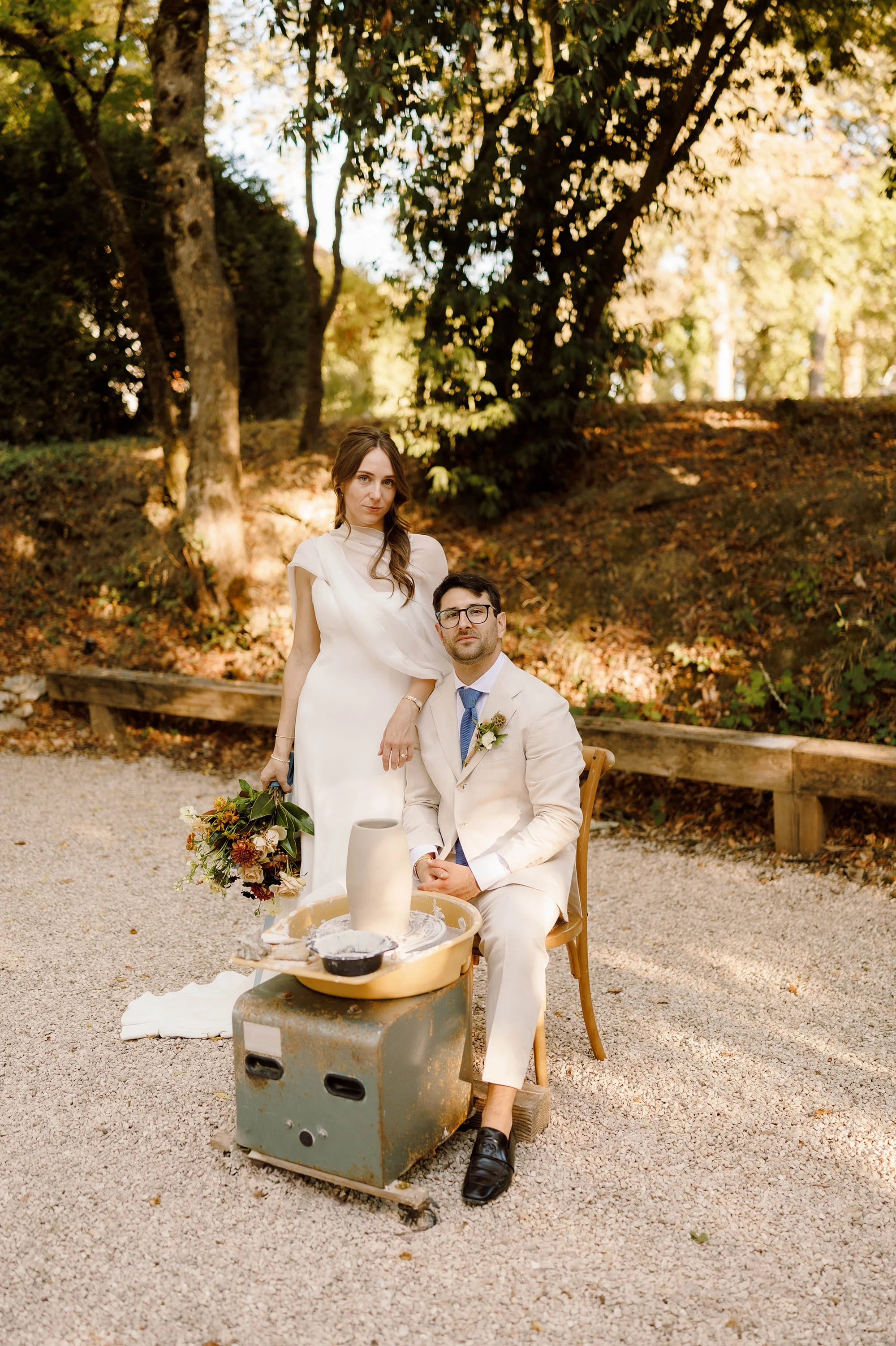bride and groom pose in front of pottery wheel owned by the groom