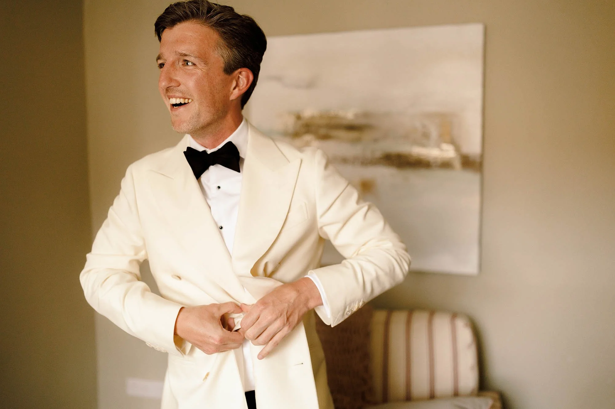 groom laughs in white tuxedo getting ready