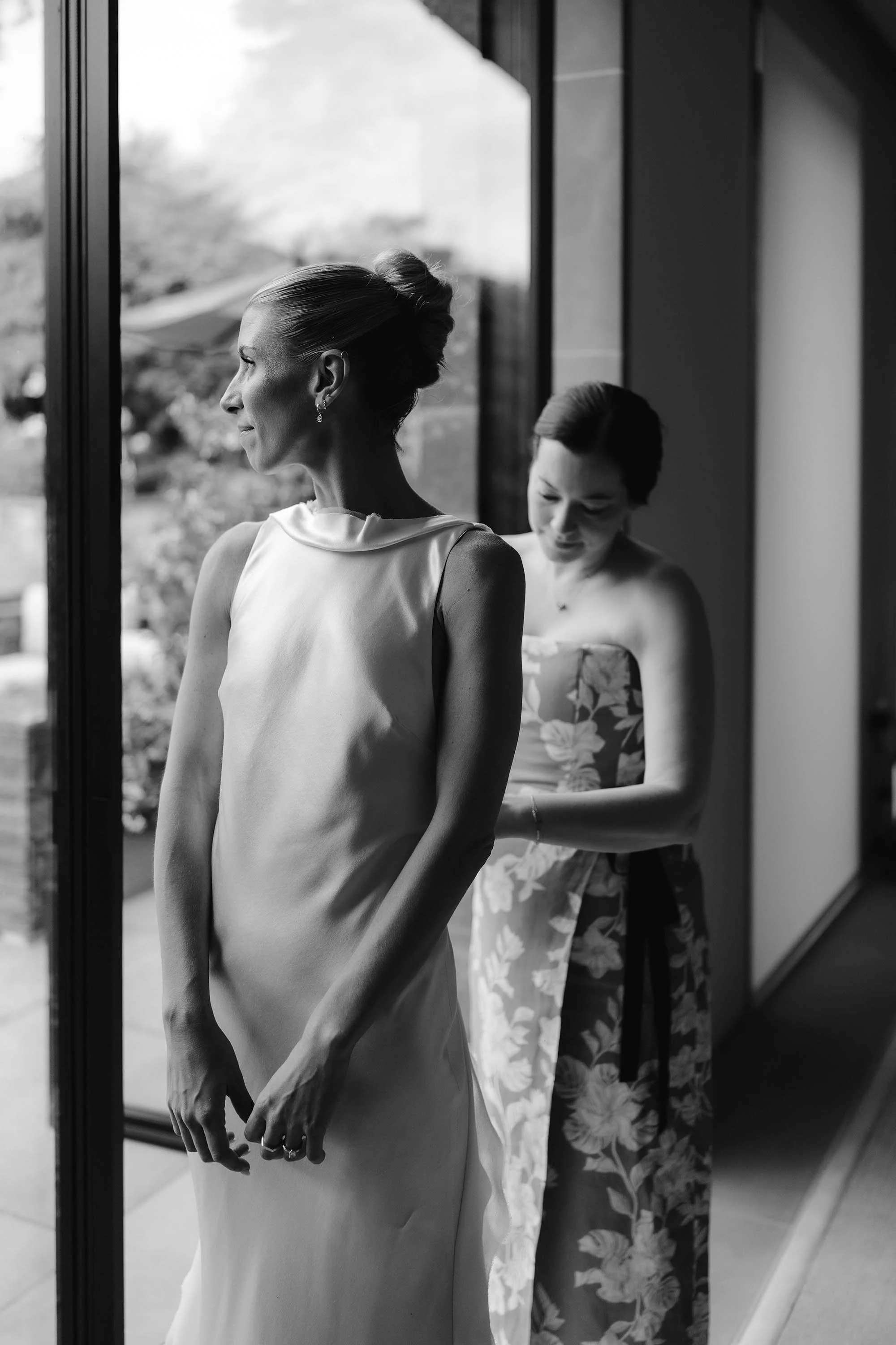 bridesmaid helps bride into danielle frankel wedding dress